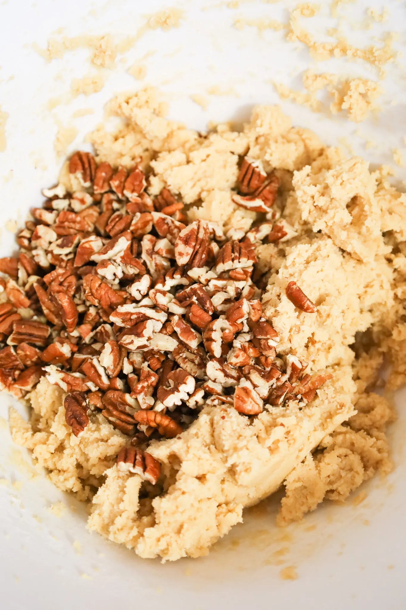 chopped pecans on top of cookie dough in a mixing bowl
