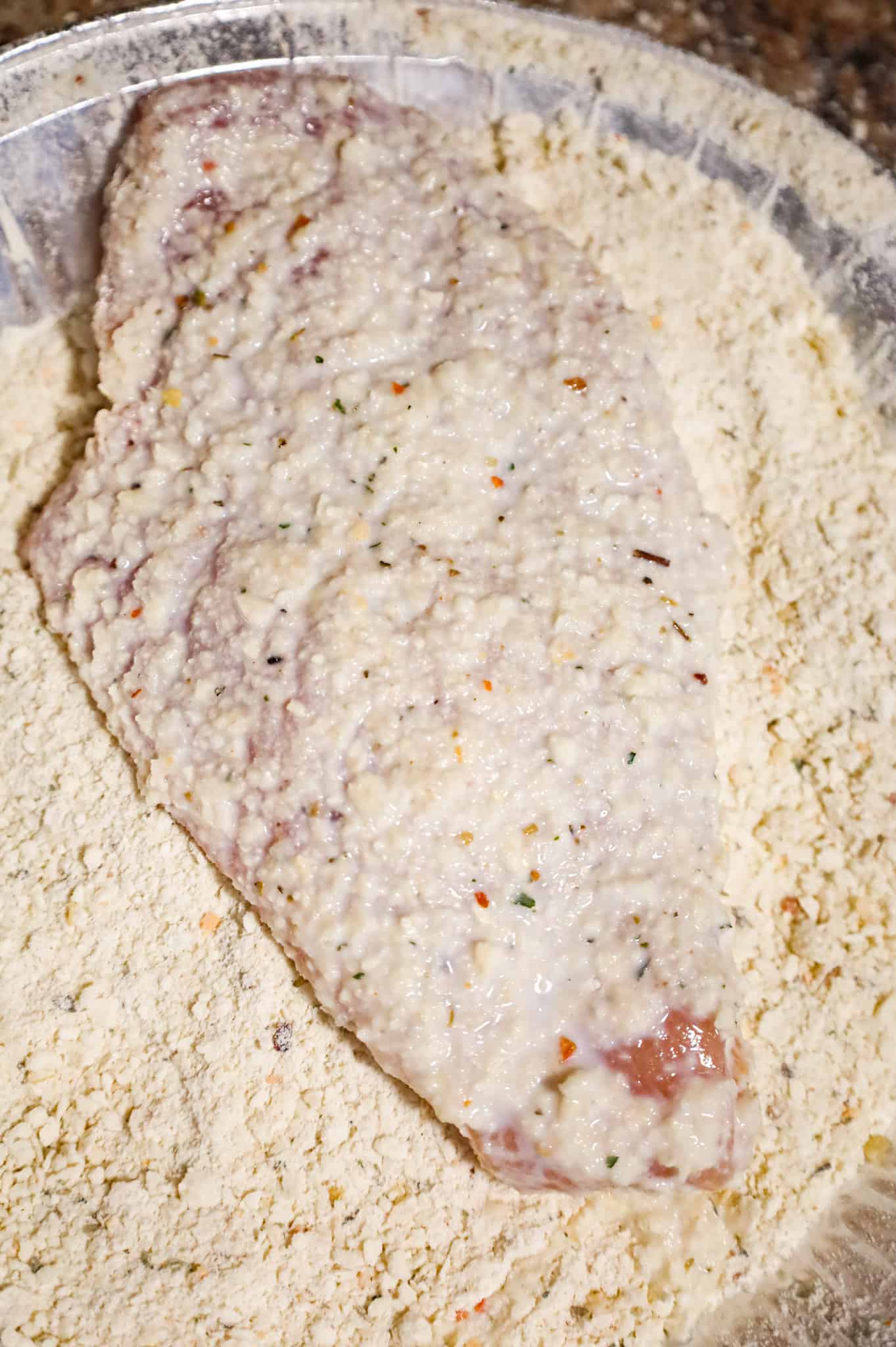 chicken breast being coated in bread crumbs