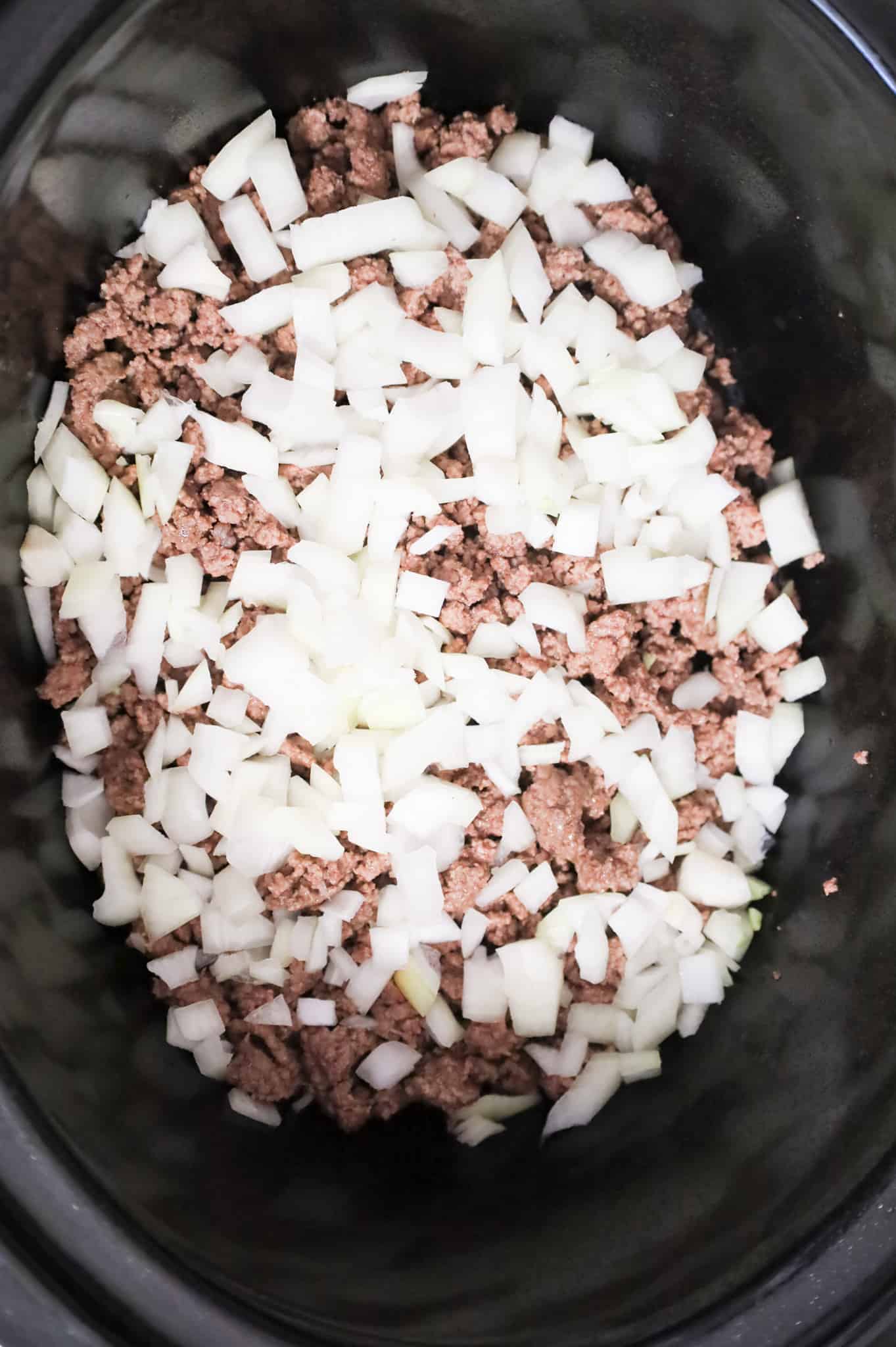 diced onions on top of cooked ground beef in the bottom of a crock pot