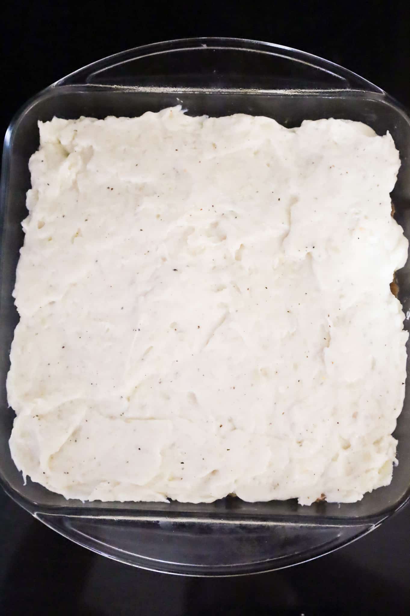 whipped potatoes spread on top of ground beef mixture in a baking dish