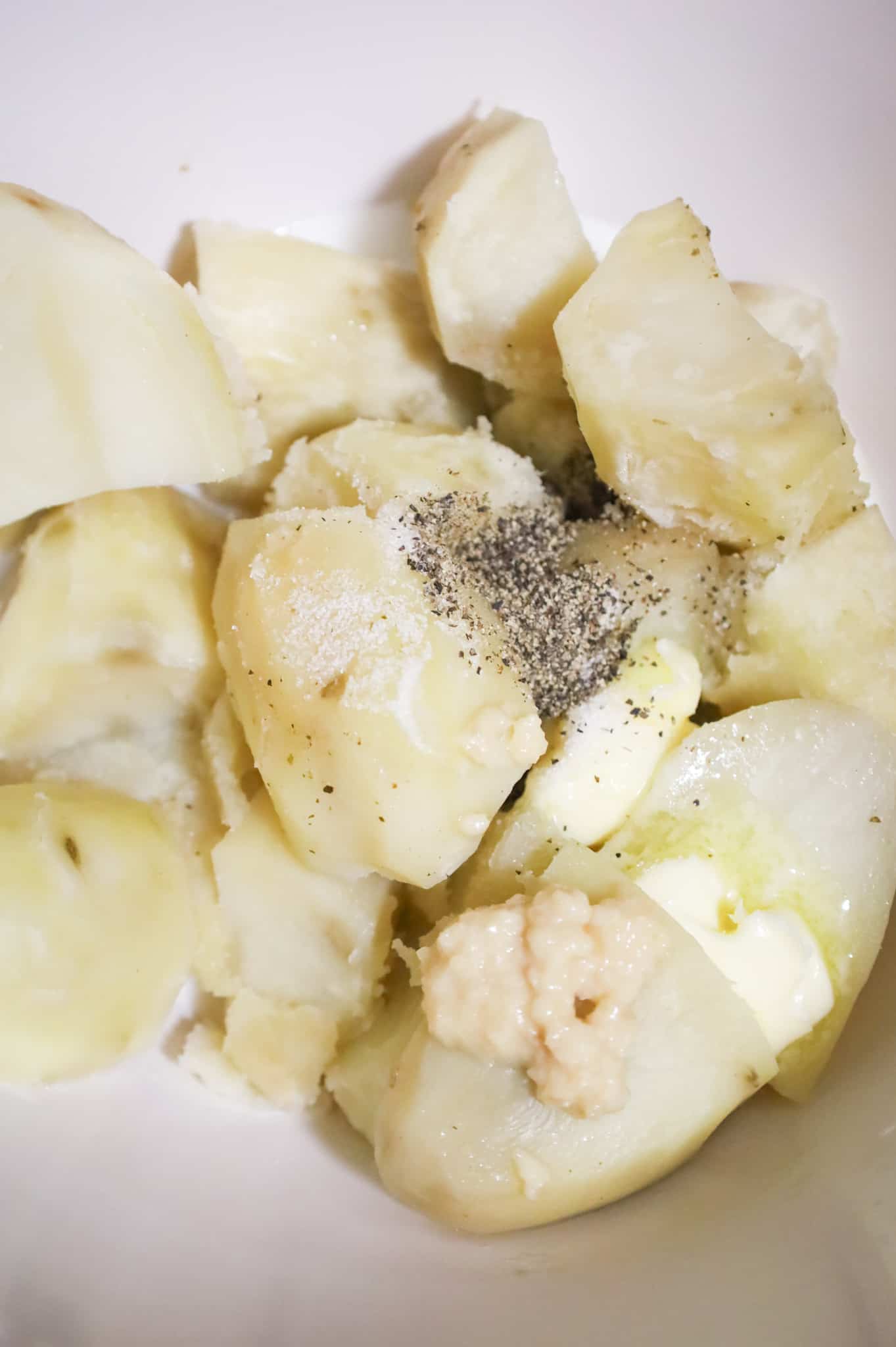salt, pepper, garlic puree, butter and milk on top of cooked potatoes in a mixing bowl