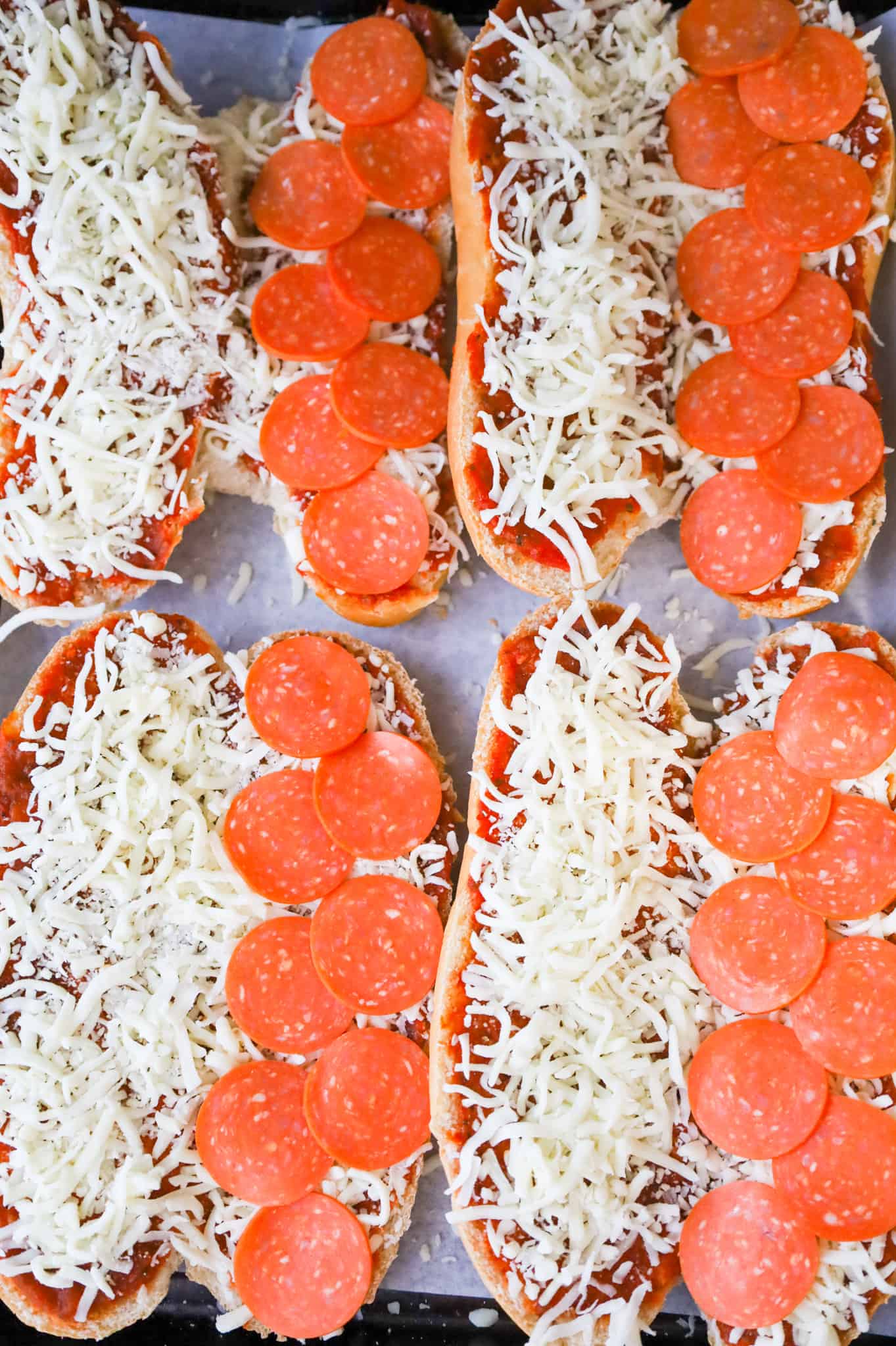 pepperoni slices on top of shredded mozzarella cheese on sub buns on a baking sheet