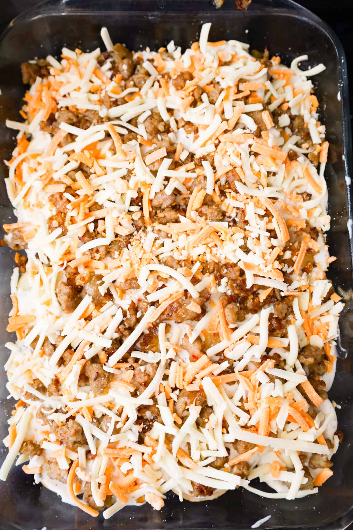 shredded cheese sprinkled over crumbled sausage and soup mixture in casserole dish