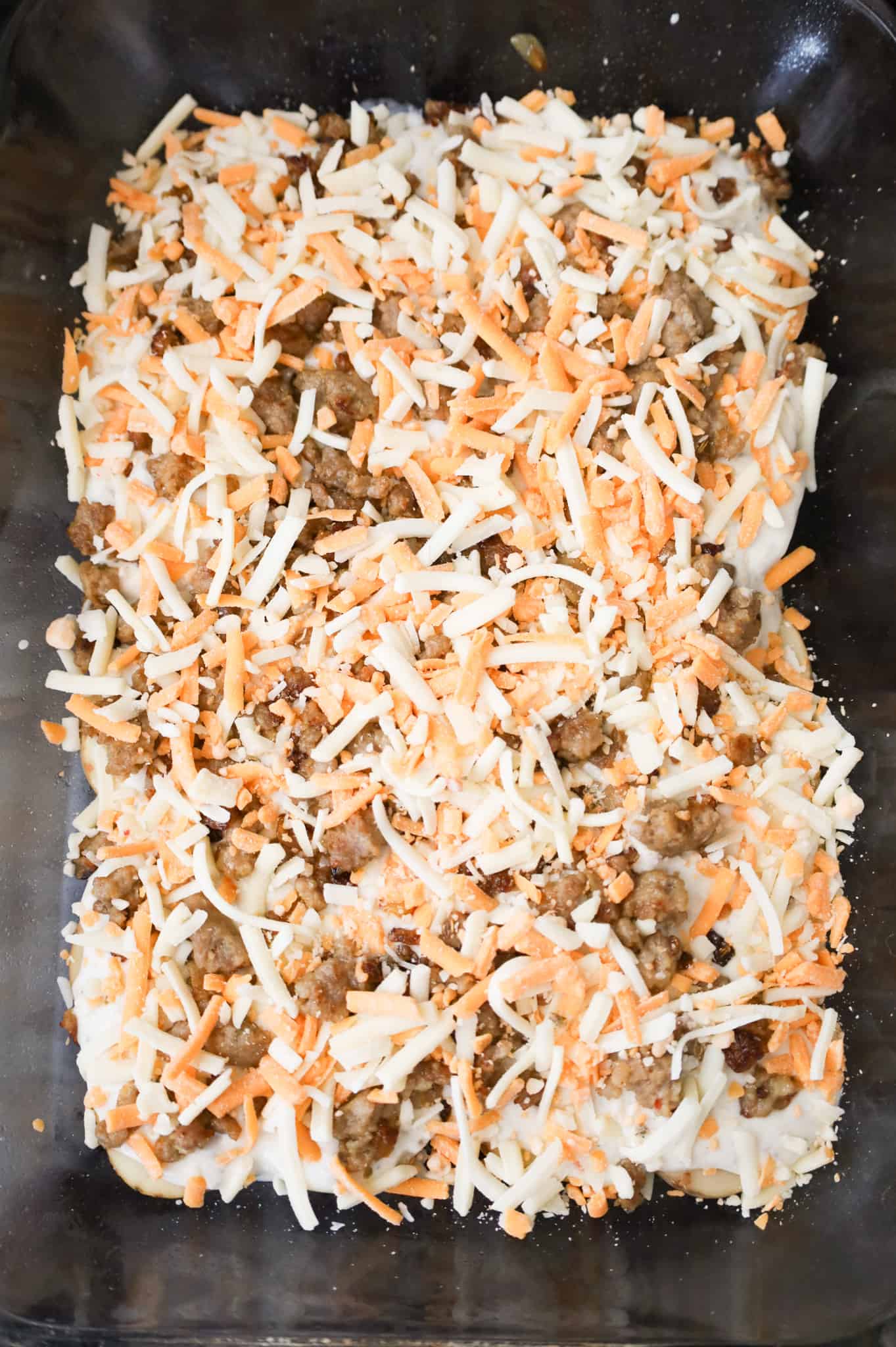 shredded cheddar and mozzarella cheese on top of crumbled Italian sausage in a baking dish