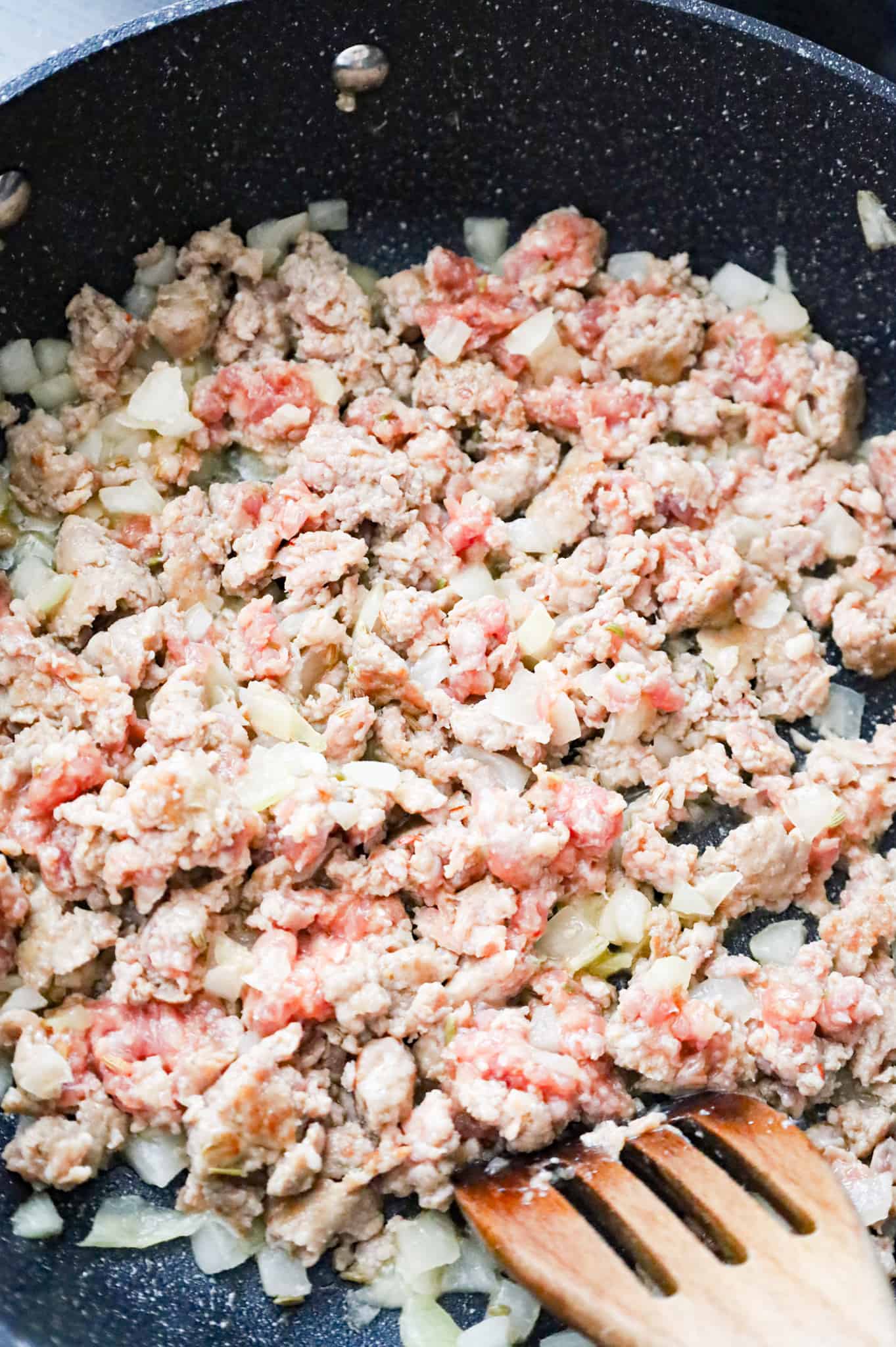 Italian sausage and diced onion cooking in a skillet