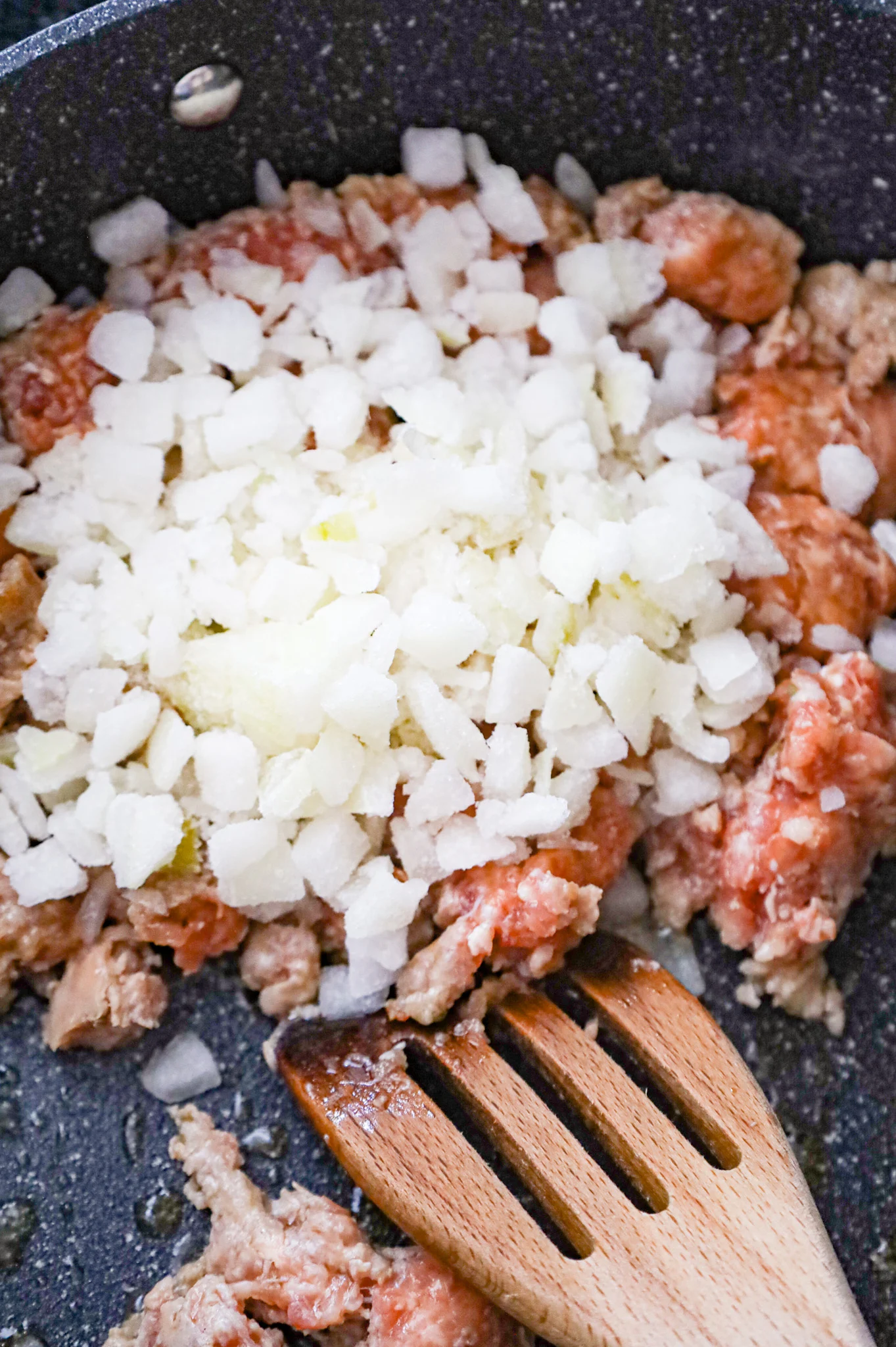 diced onions on top of Italian sausage meat in a skillet
