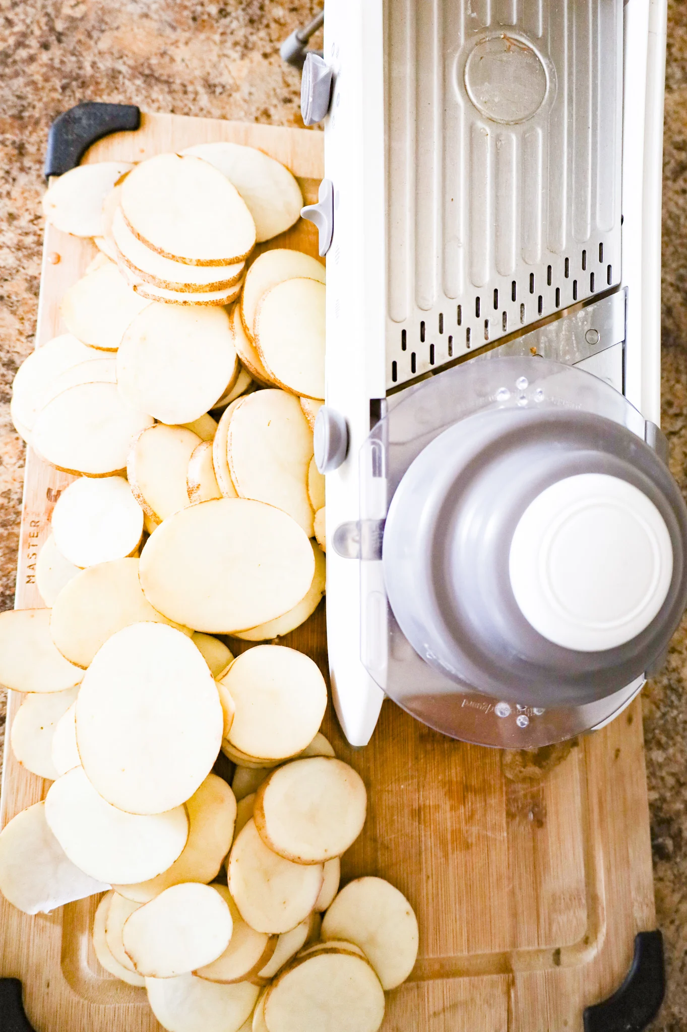 sliced potatoes on a cutting board with a mandoline slicer