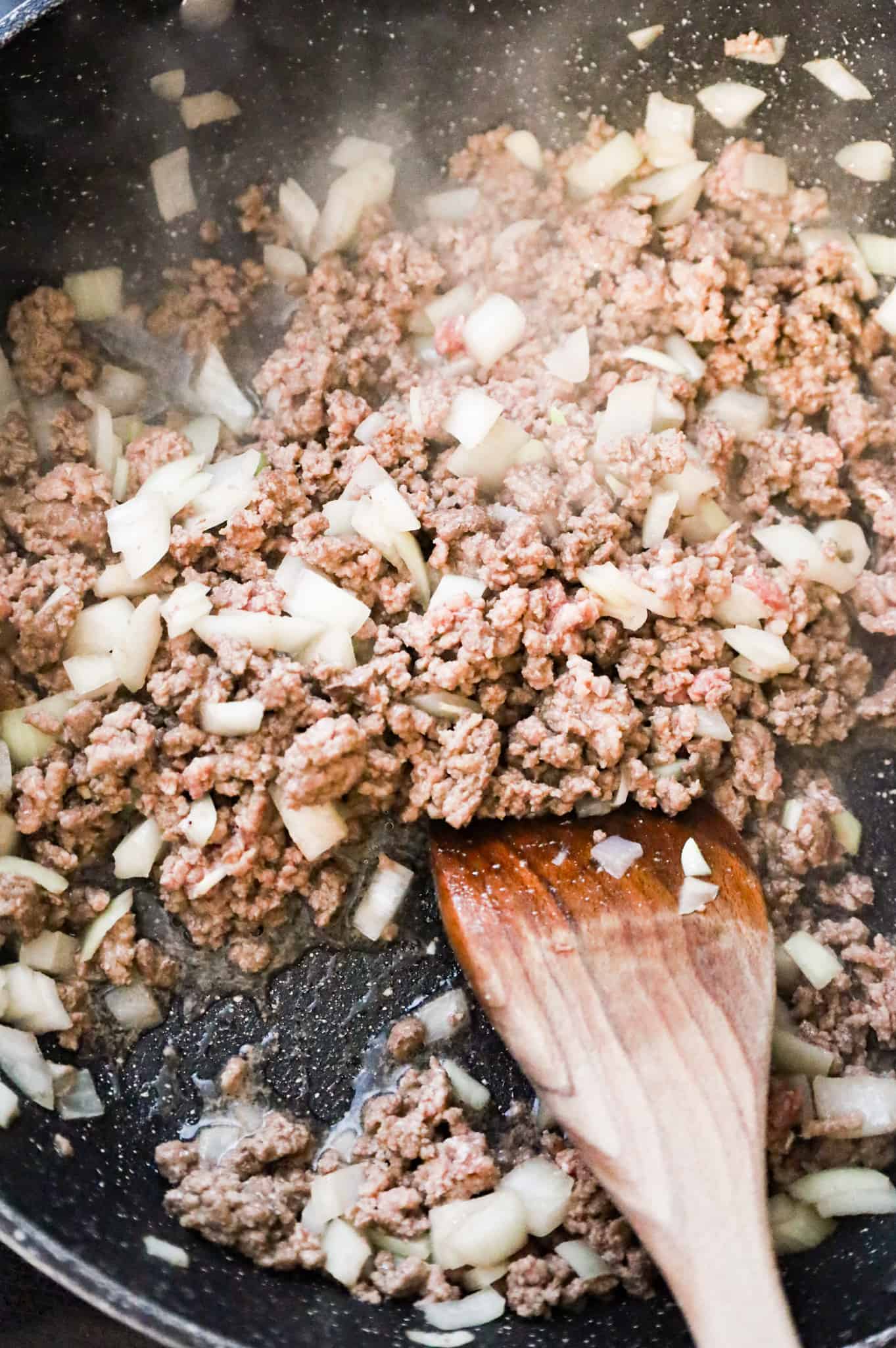 crumbled beef and diced onions cooking in a skillet