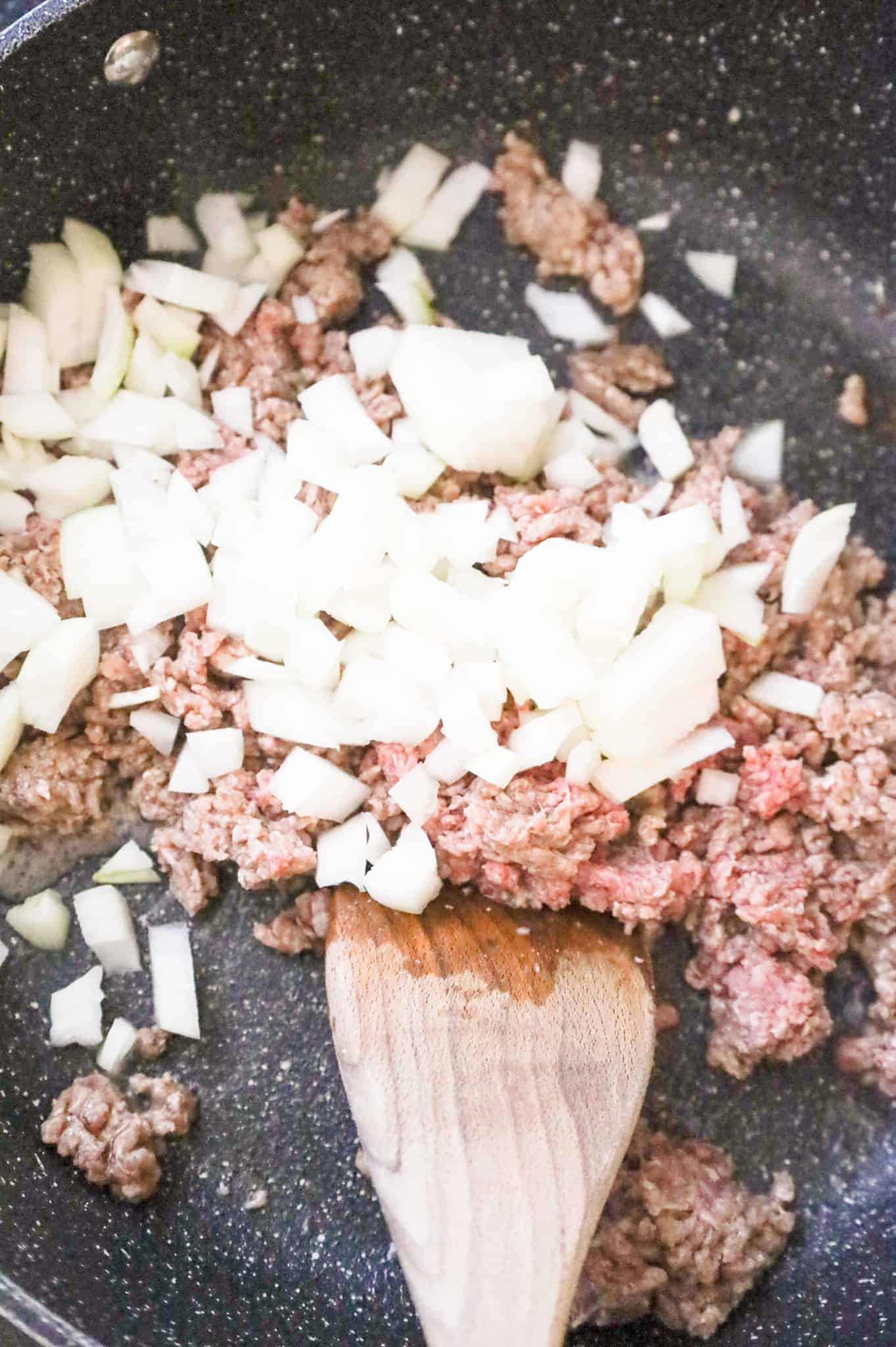 ground beef and diced onions cooking in a skillet