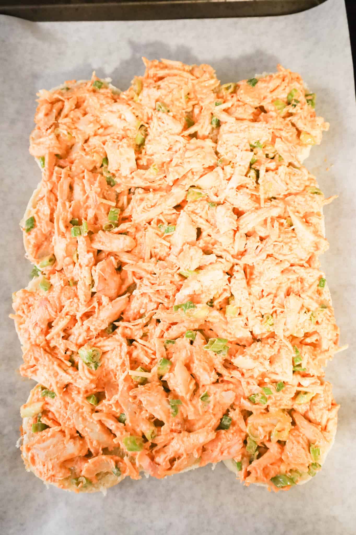 shredded Buffalo chicken mixture on top of dinner rolls on a baking sheet