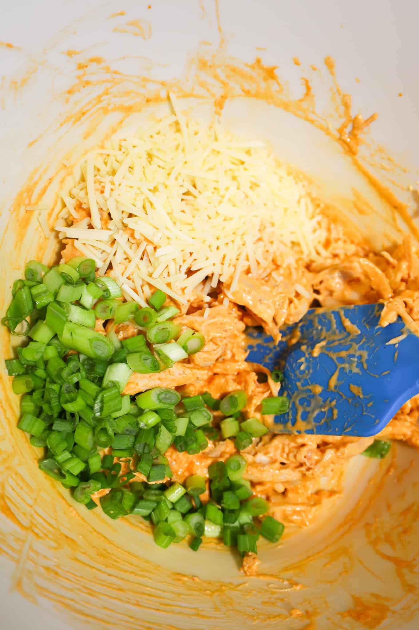 chopped green onions and shredded parmesan on top of shredded Buffalo chicken in a mixing bowl