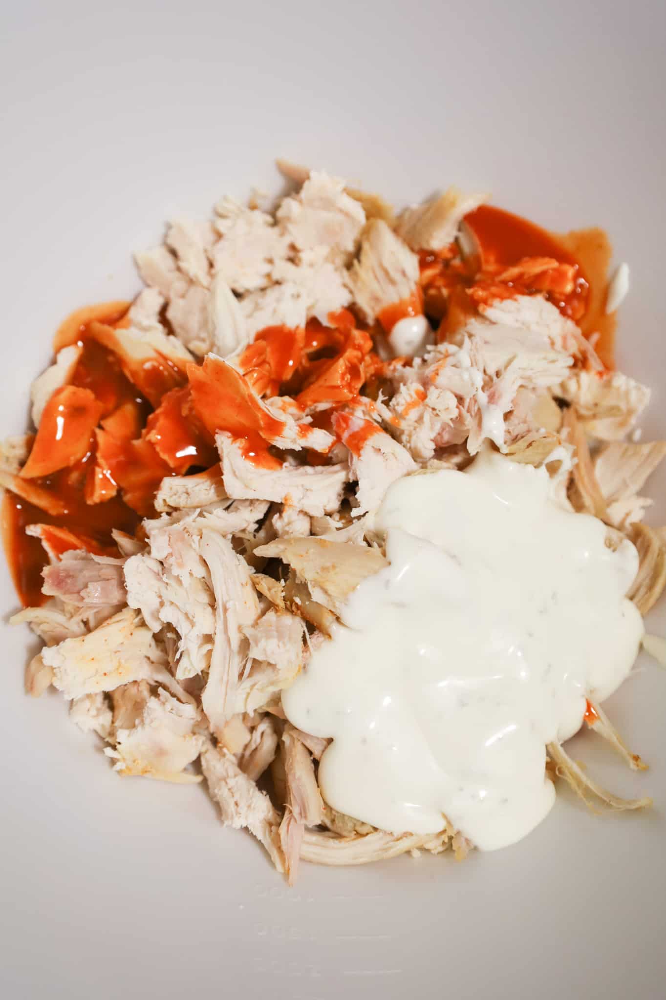 Buffalo sauce and ranch dressing on top of shredded chicken in a mixing bowl