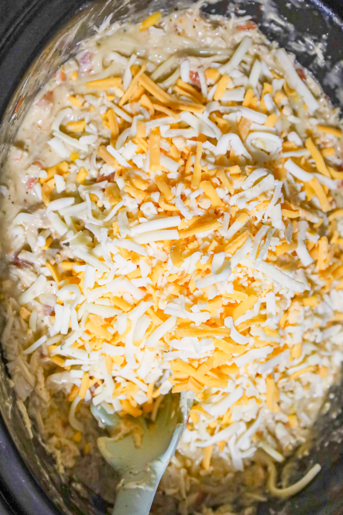 shredded cheese on top of creamy spaghetti in a crock pot