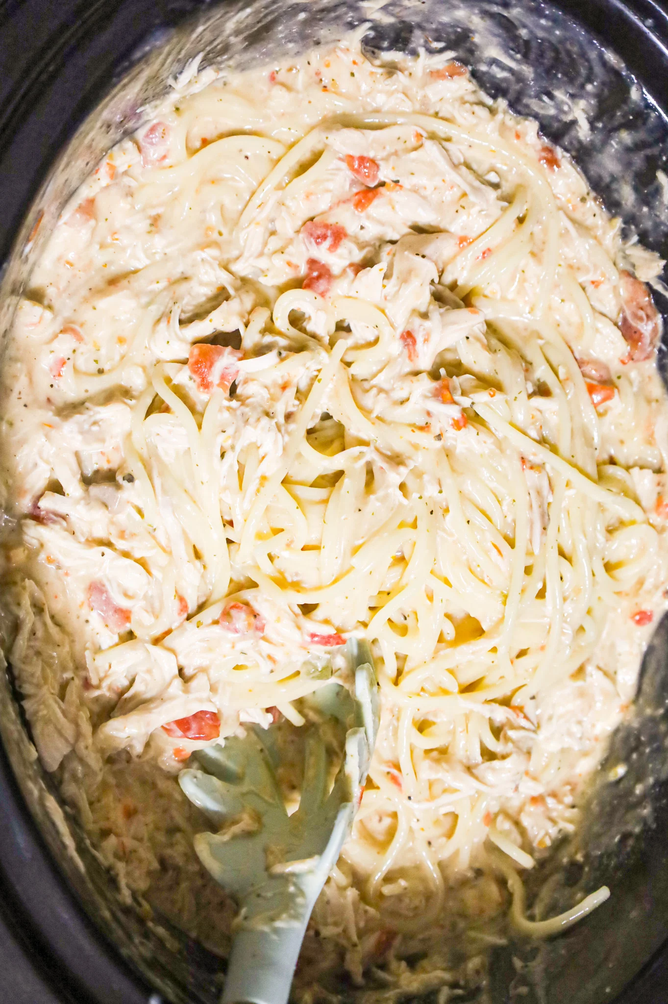 cooked spaghetti being stirred into a cream soup and cream cheese mixture in a crock pot