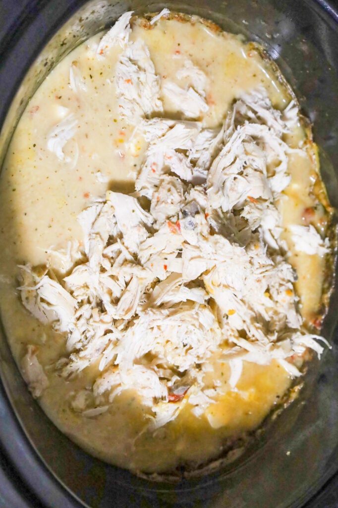 shredded chicken on top cream soup mixture in a crock pot of cream soup mixture in