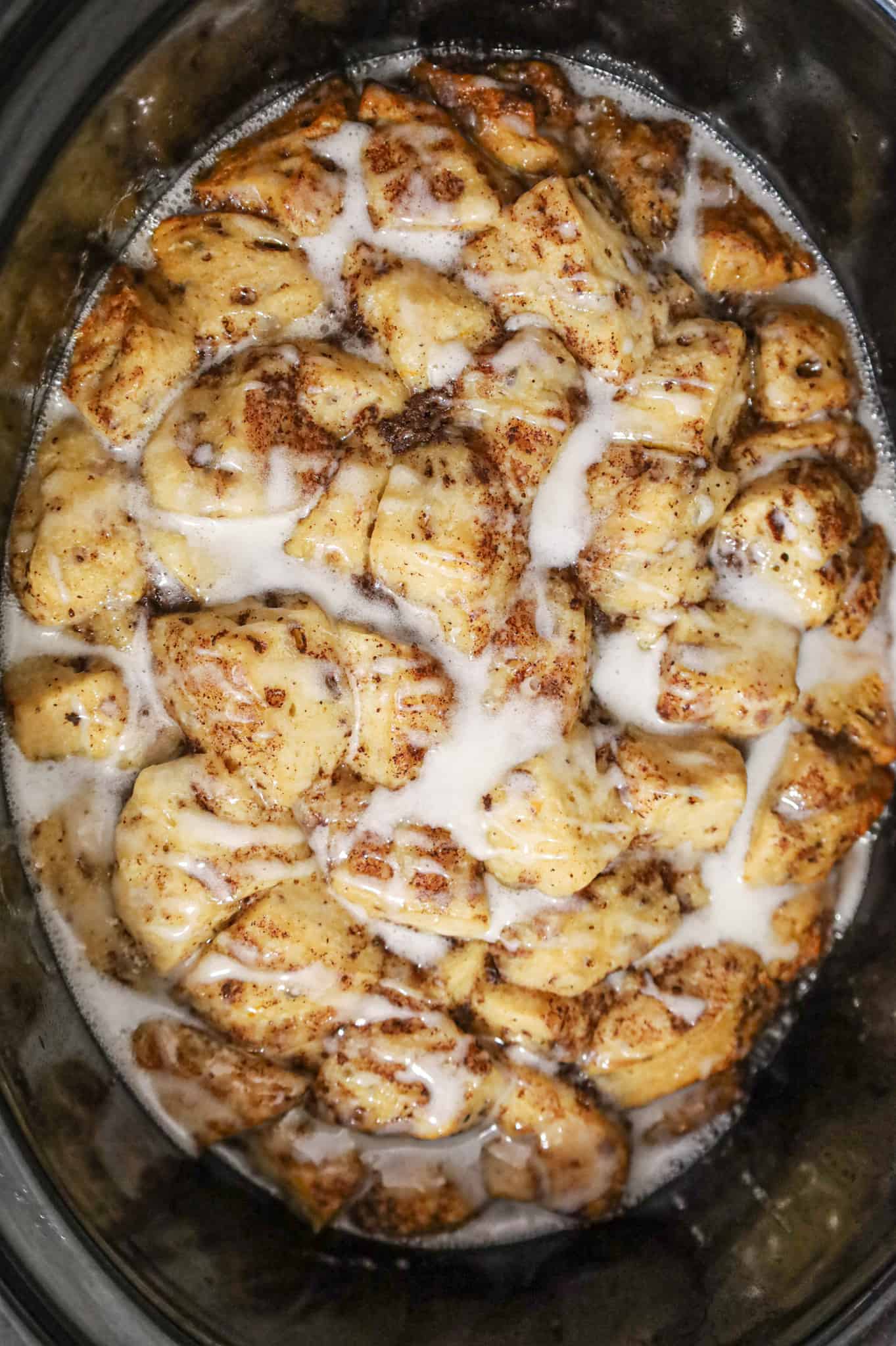 cinnamon roll icing drizzled over cooked cinnamon roll casserole in a crock pot