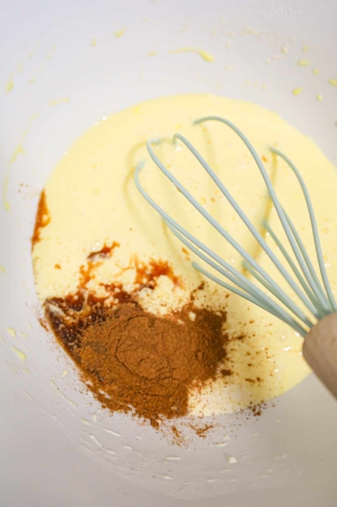 cinnamon and vanilla extract added to cream and egg mixture in a mixing bowl