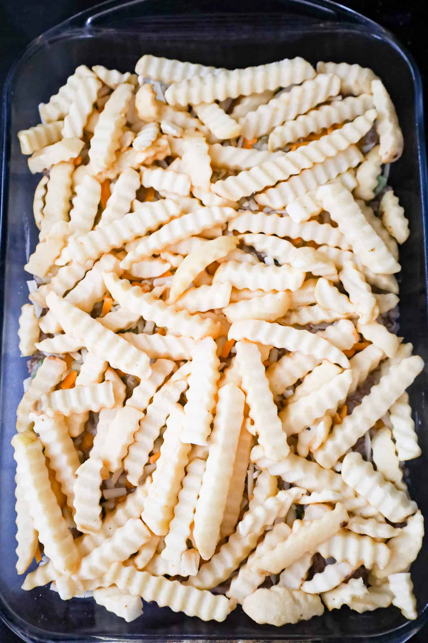 frozen crinkle cut fries on top of ground beef mixture in a baking dish