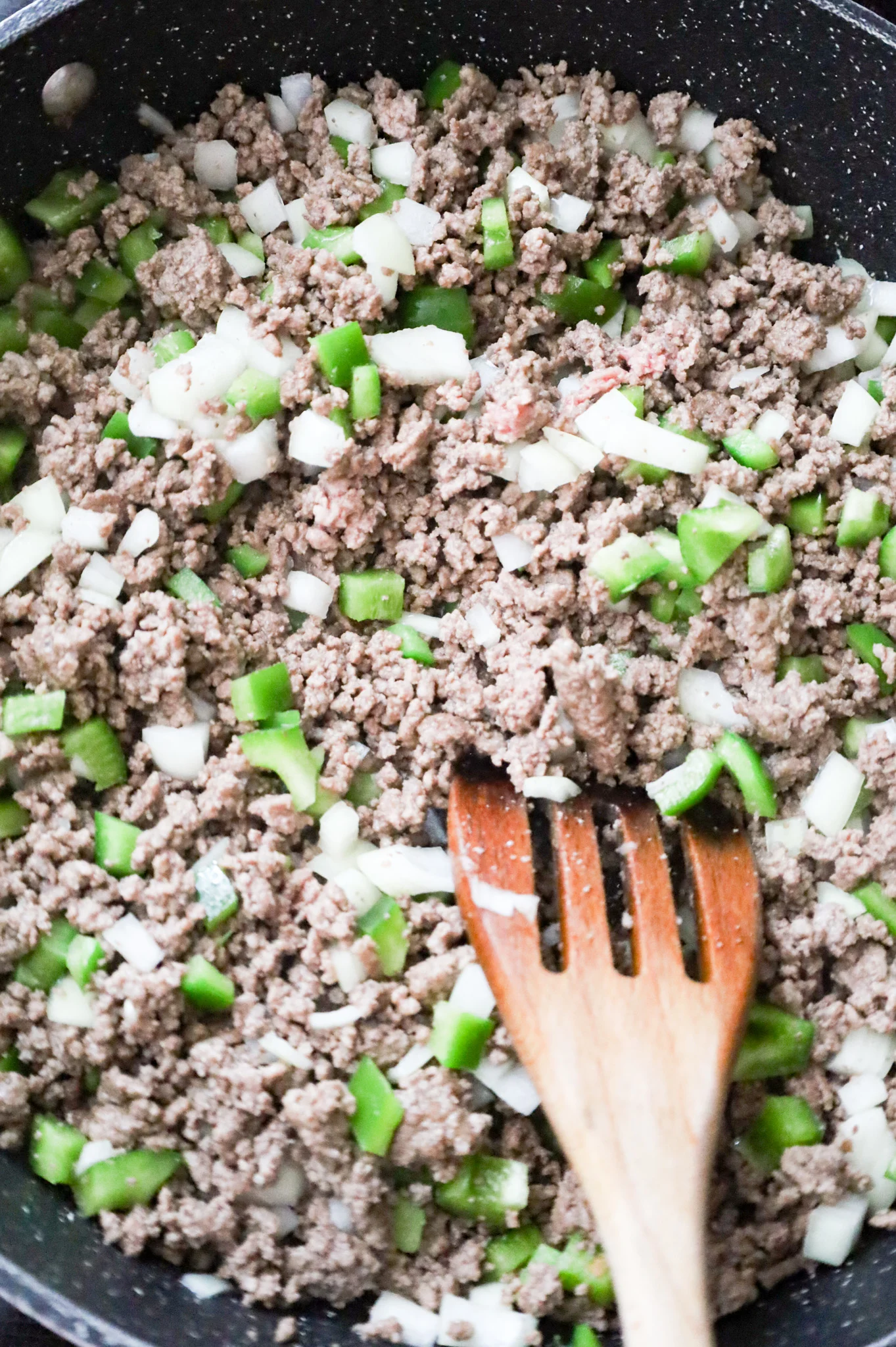 stirring diced onions and diced green peppers into cooked ground beef in a skillet