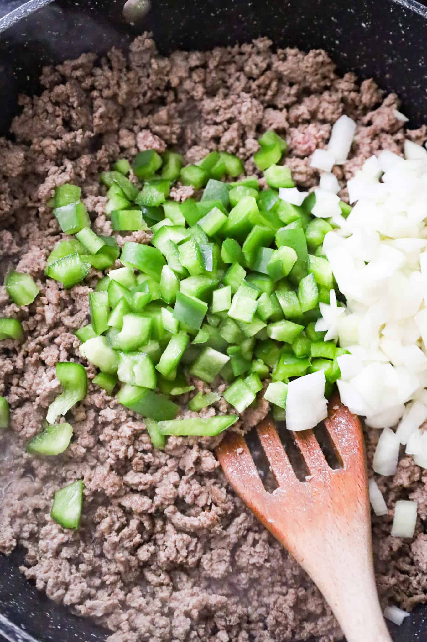 diced green pepper and diced onions on top of cooked ground beef in a skillet