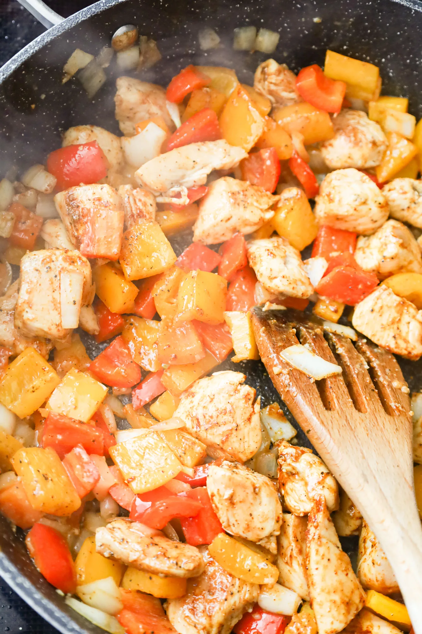 diced peppers and chicken breast chunks being stirred with spices in a skillet