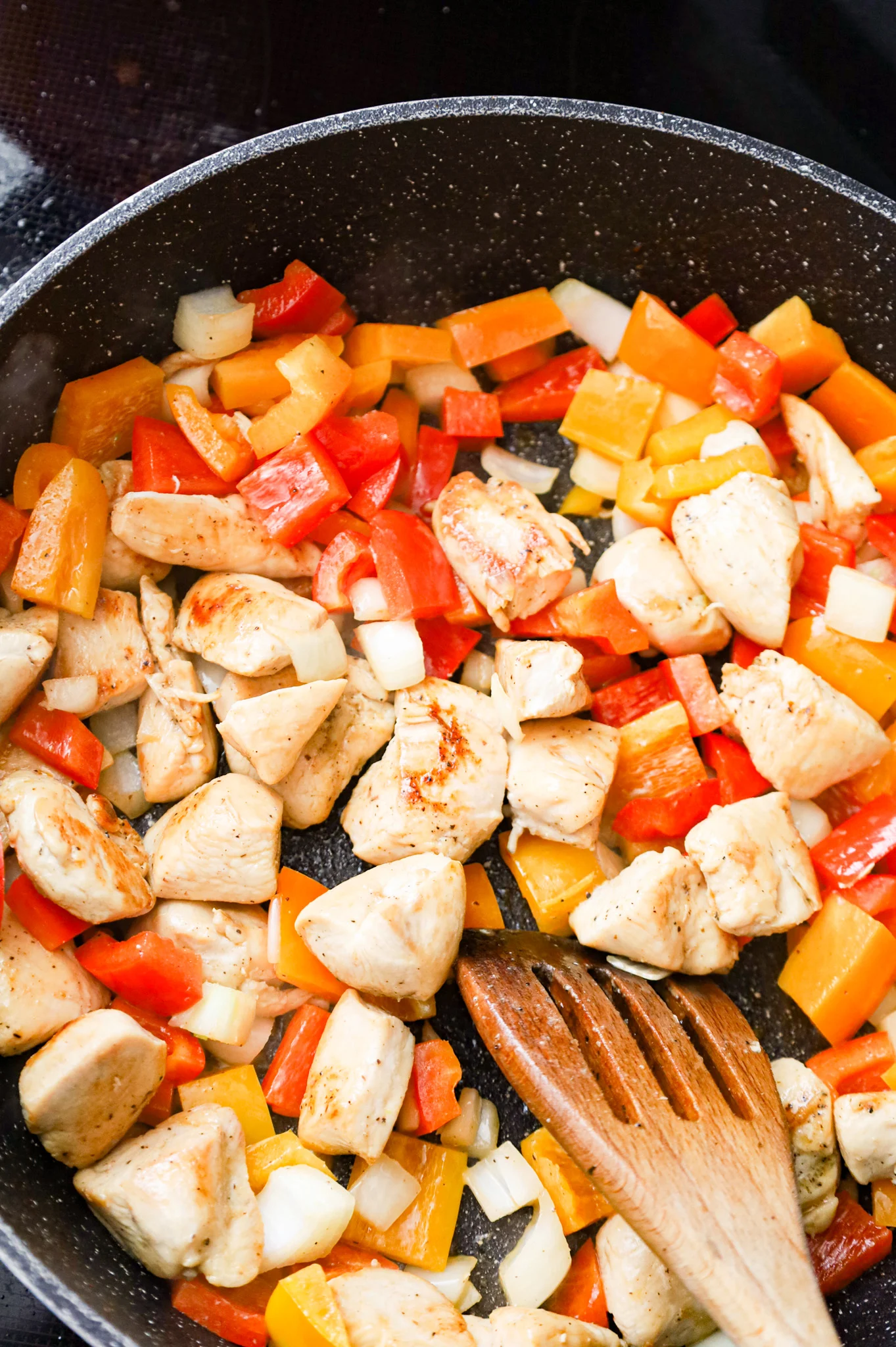 chicken breast chunks and diced peppers being stirred together in a skillet