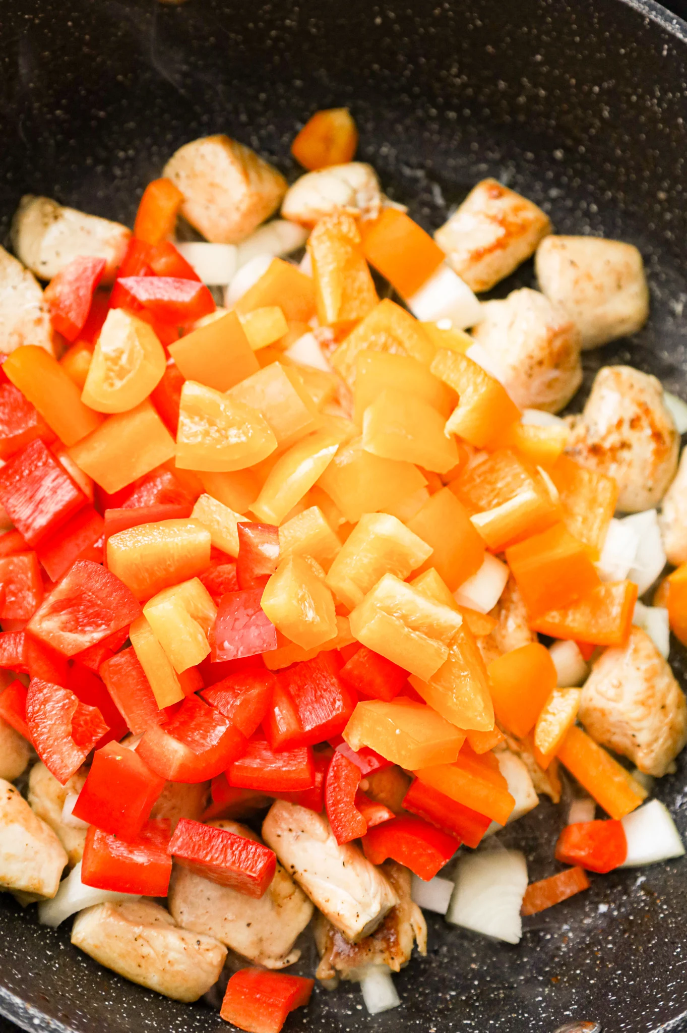 diced onions and diced bell peppers added to a skillet with cooked chicken breast chunks