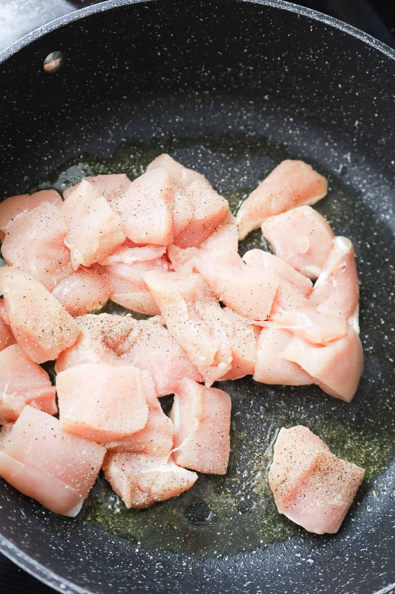 salt and pepper sprinkled on chicken breast chunks in a skillet