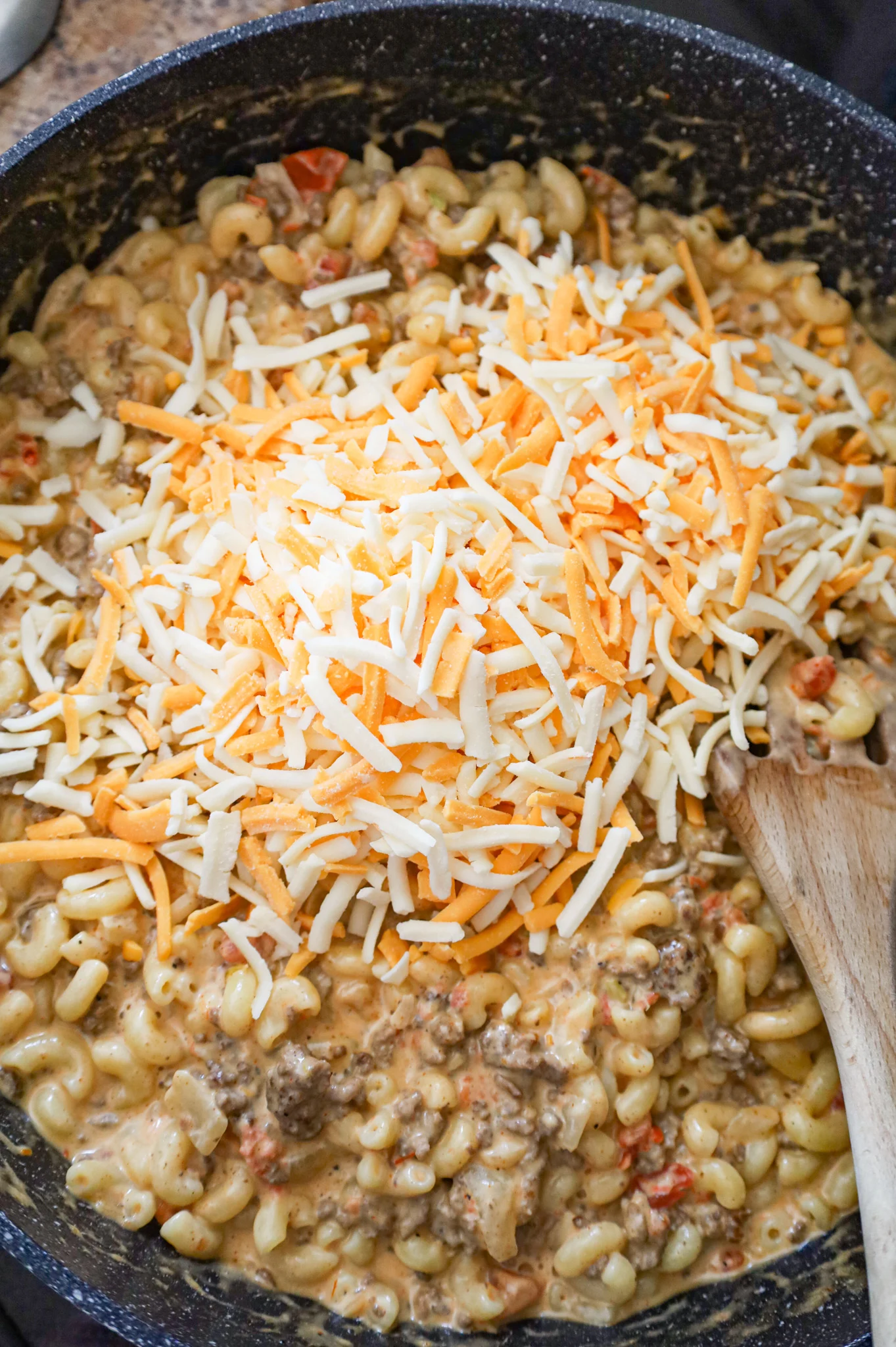 shredded cheese on top of ground beef macaroni in a skillet