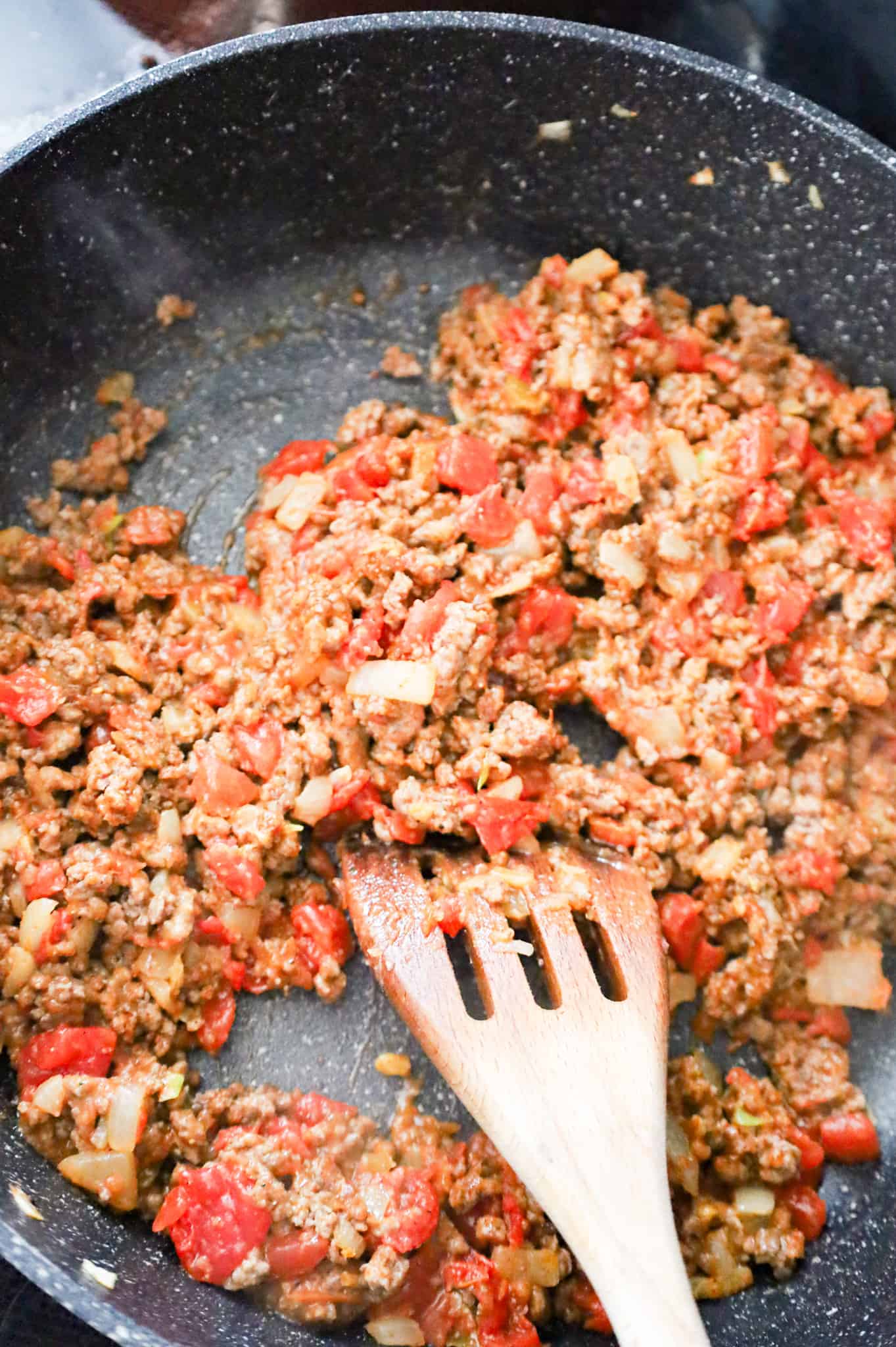 cooked ground beef, diced onions and Rotel being stirred in a skillet