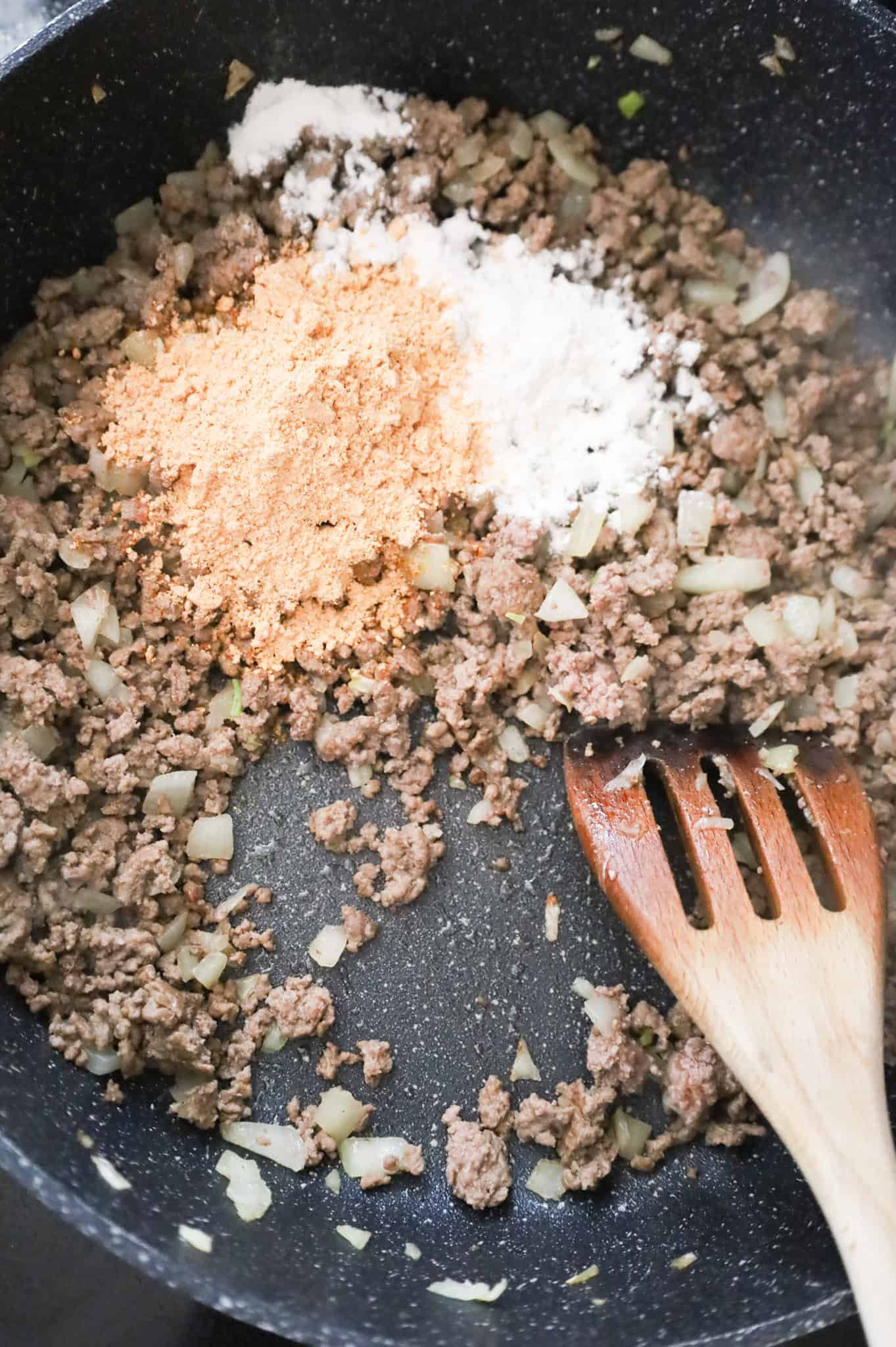 taco seasoning and all purpose flour on top of cooked ground beef and diced onions in a skillet