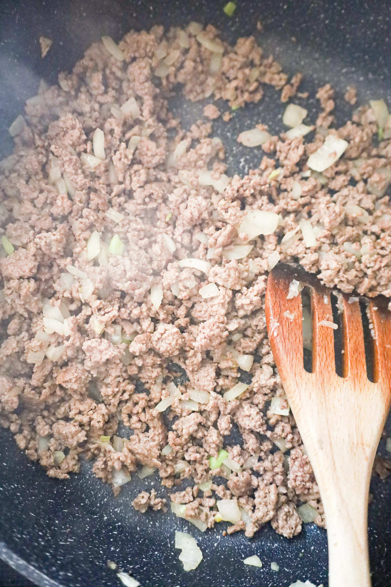 ground beef and diced onions cooking in a skillet