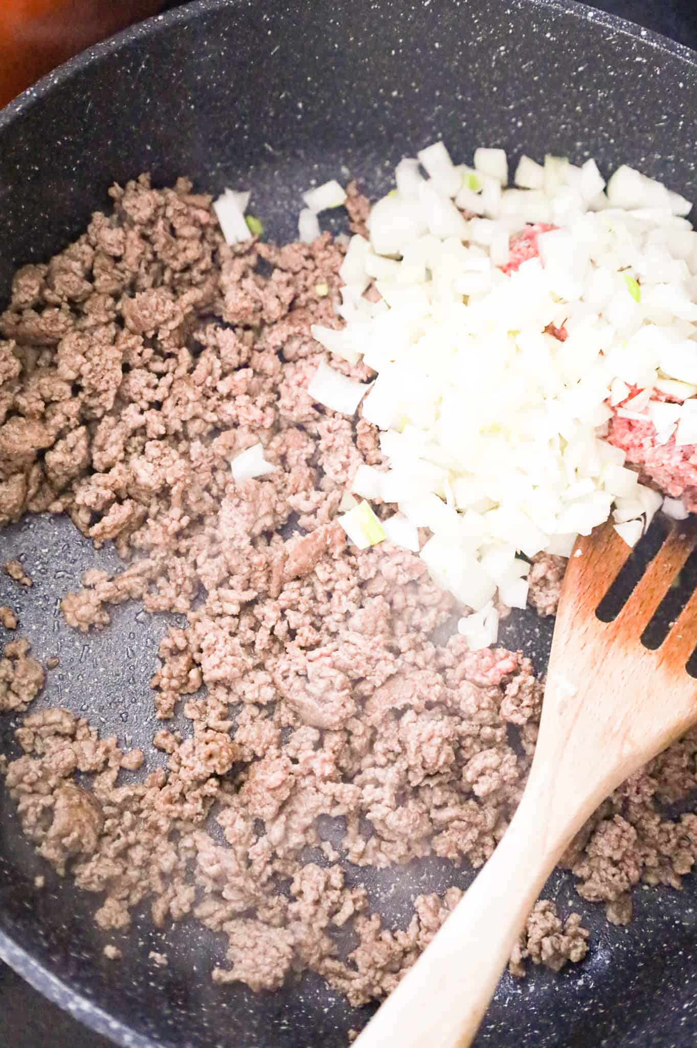 diced onions on top of crumbled ground beef in a skillet