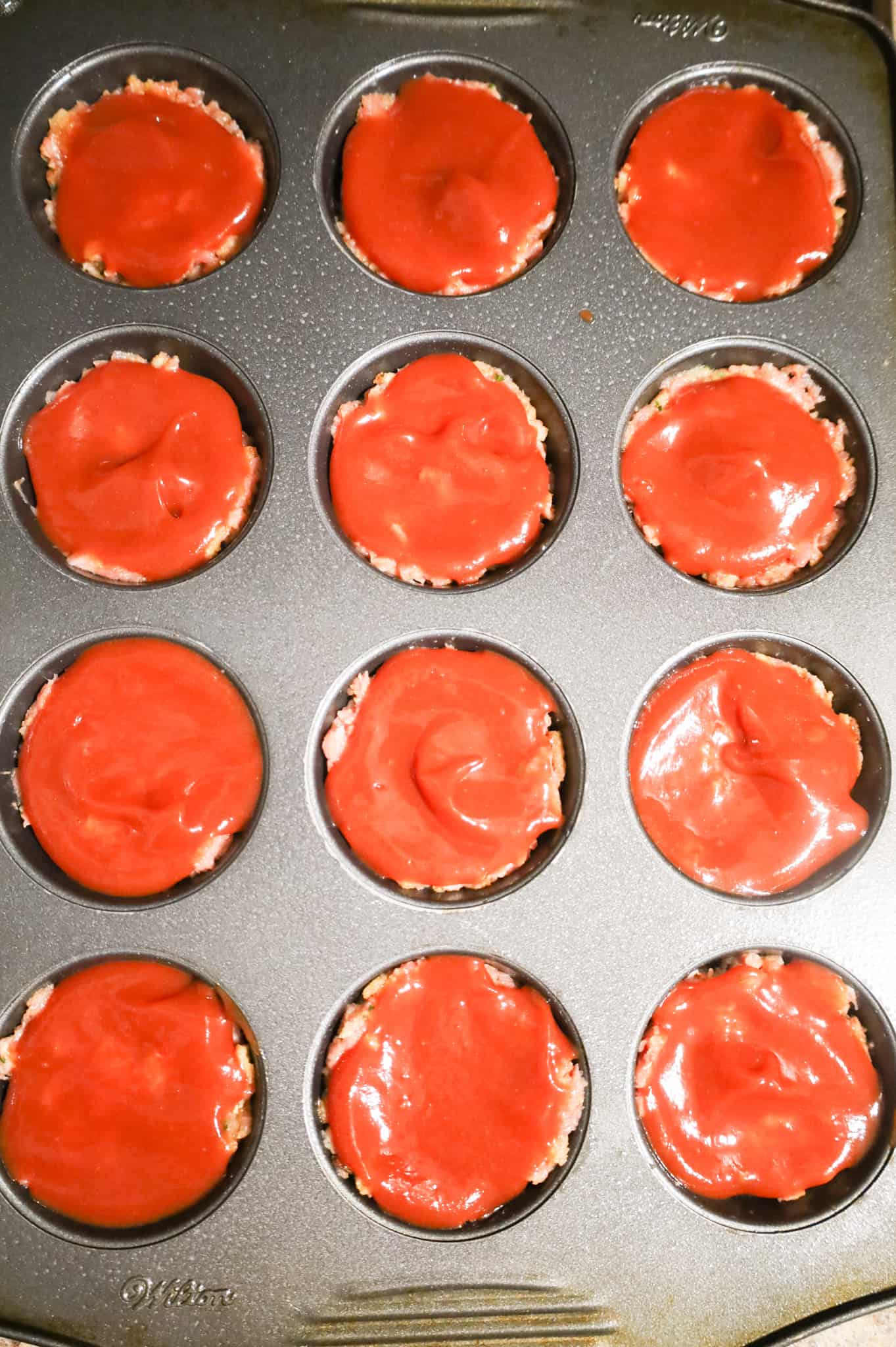 ketchup sauce mixture spread on top of turkey meatloaves in a muffin tin