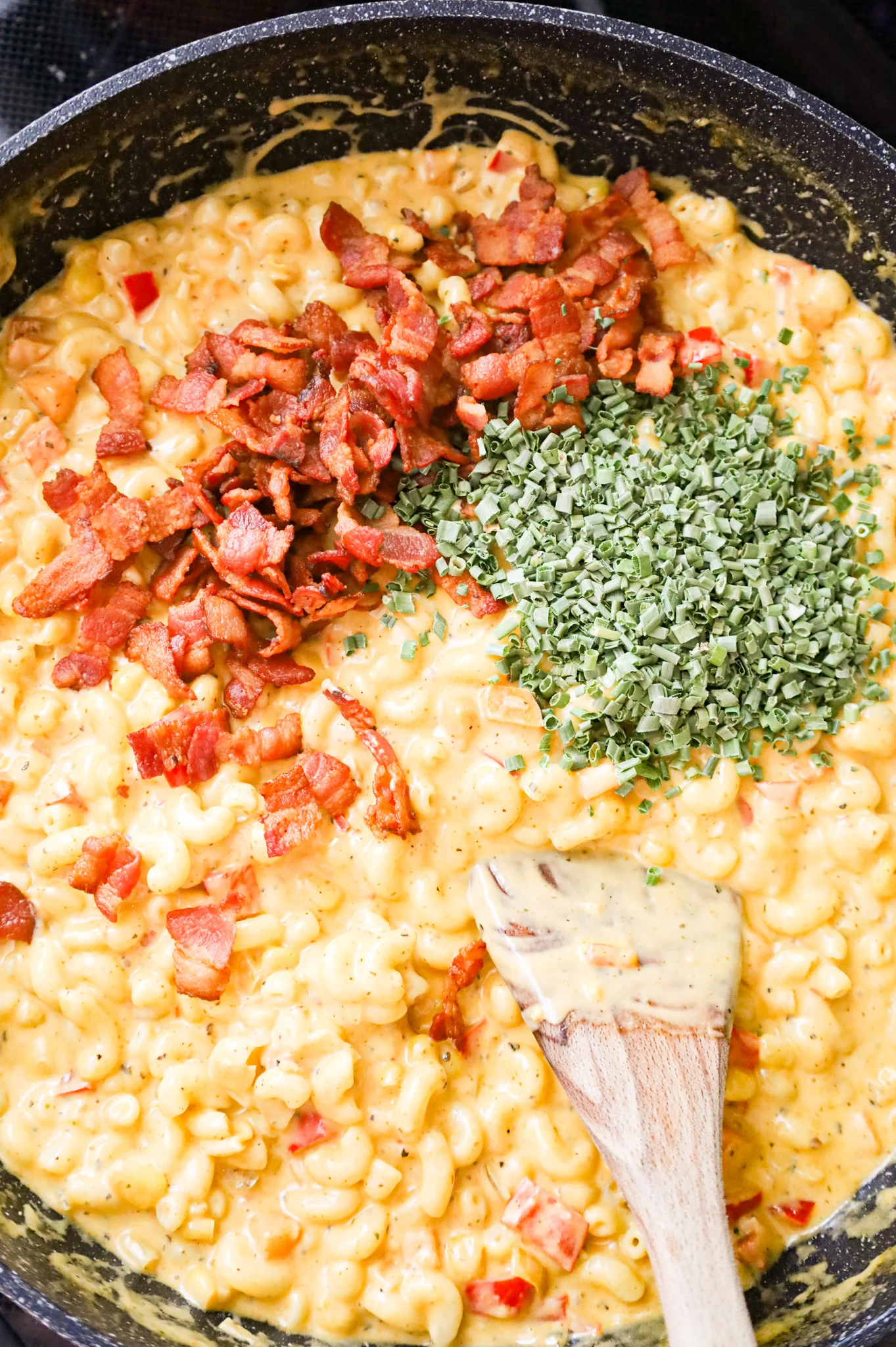 crispy bacon pieces and chopped chives added to mac and cheese in a skillet