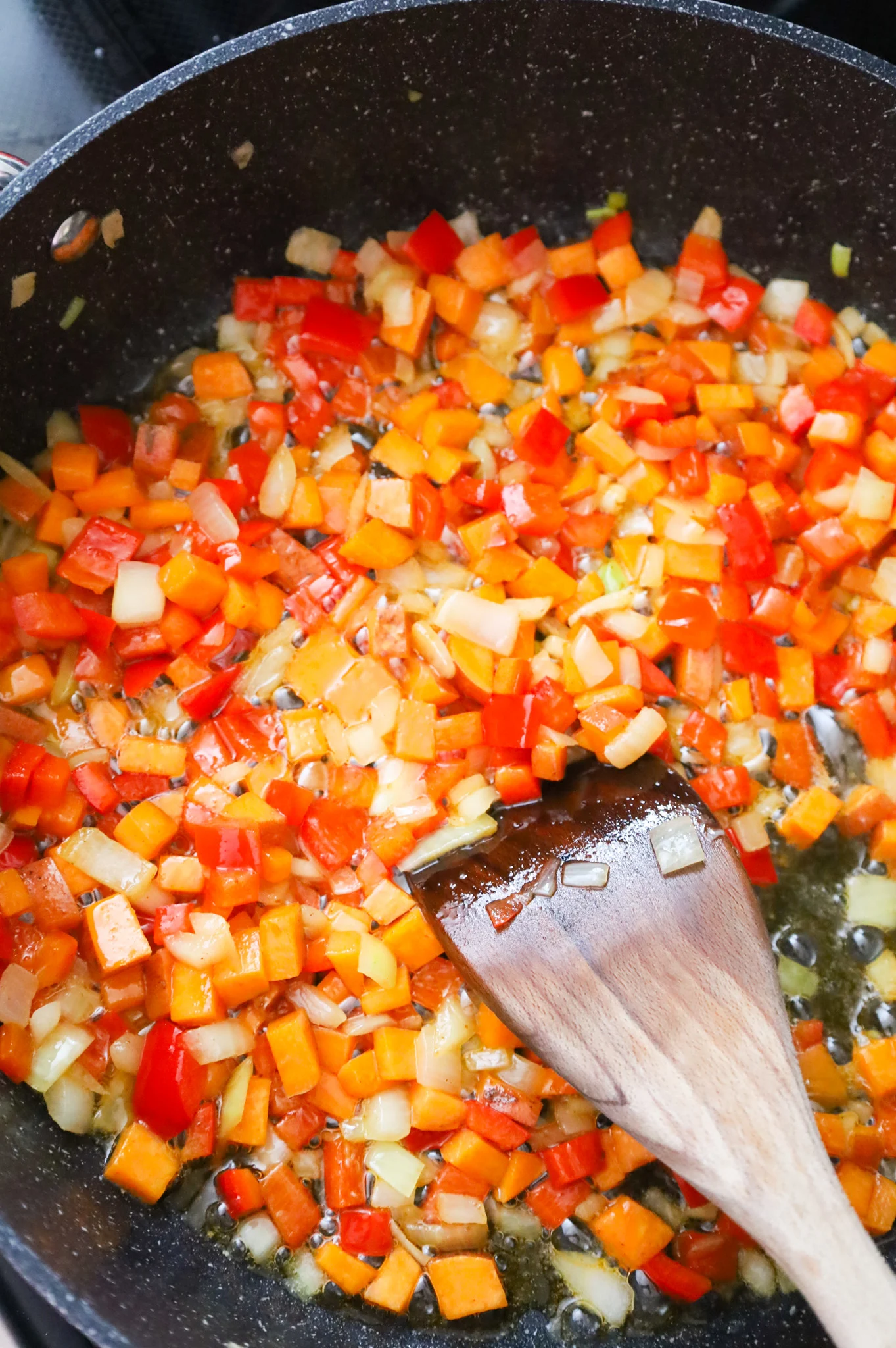 diced onions, peppers and sweet potatoes cooking in a bacon grease in a skillet