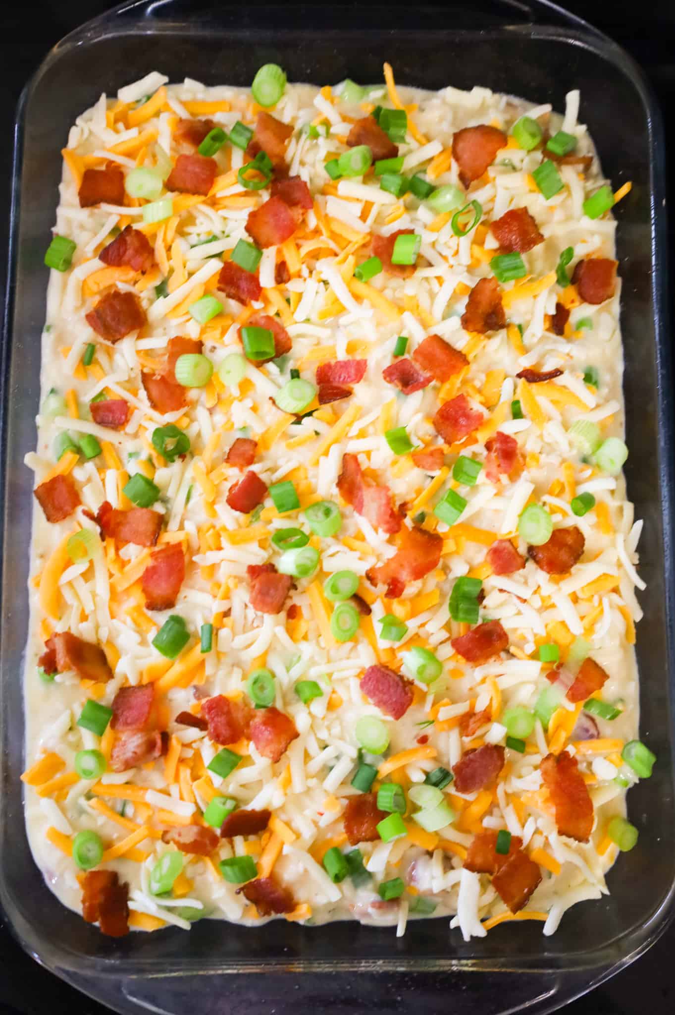 chopped bacon, green onions and shredded cheese on top of chicken bacon rice mixture in a baking dish