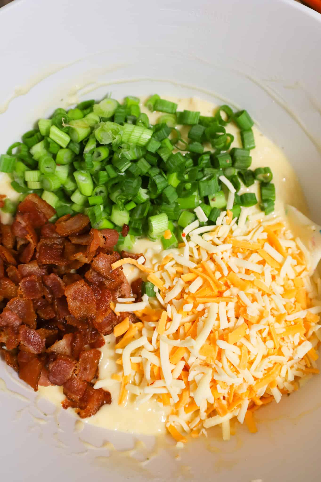 cooked bacon pieces, chopped green onions and shredded cheese on top of creamy chicken mixture in a mixing bowl