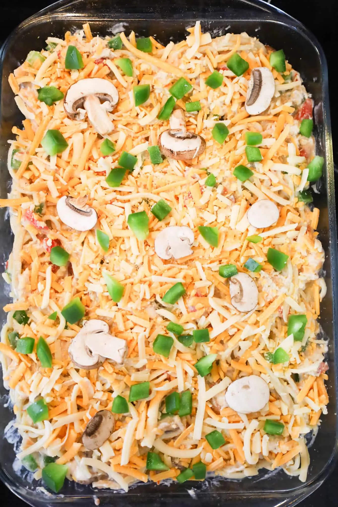 diced green peppers and sliced mushrooms on top of cheesy chicken spaghetti in a baking dish