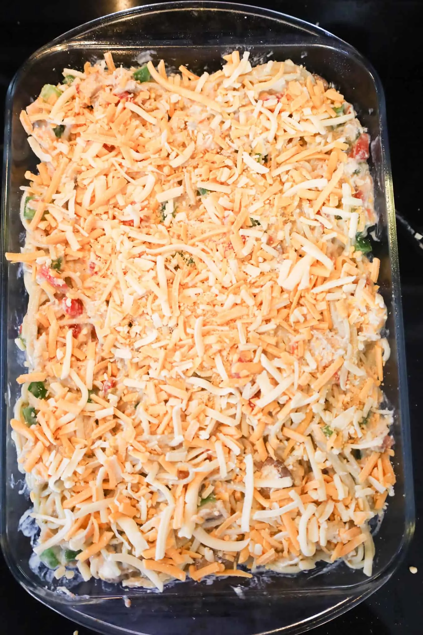 shredded cheese on top of creamy chicken spaghetti in a baking dish