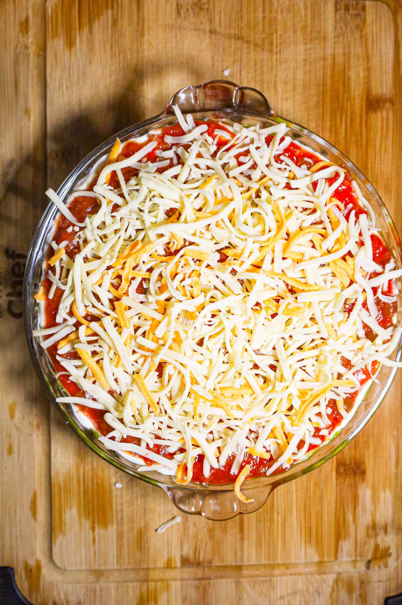 shredded cheese blend on top of nacho dip in a pie plate