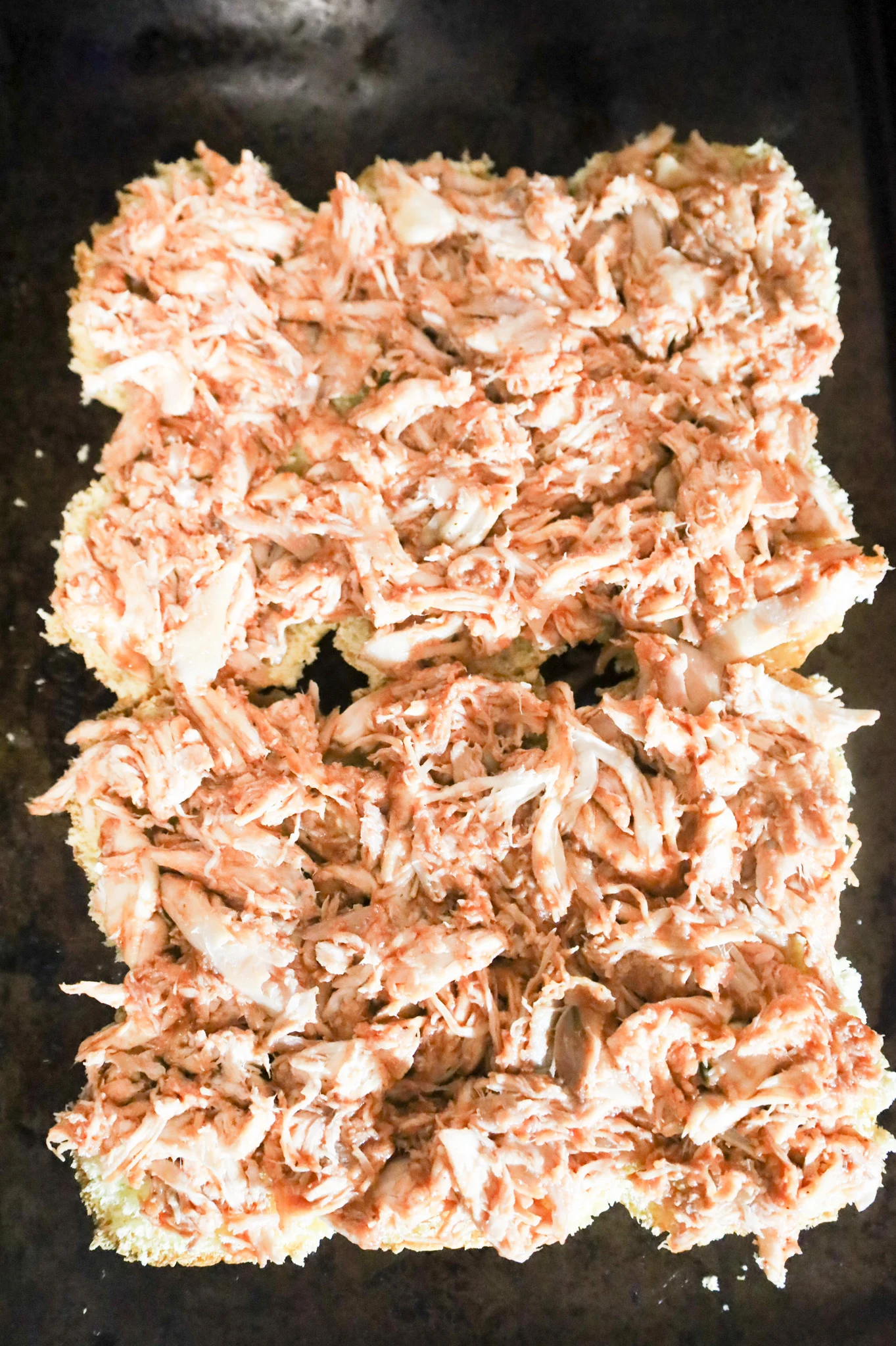 shredded bbq chicken on top of dinner rolls on a baking sheet