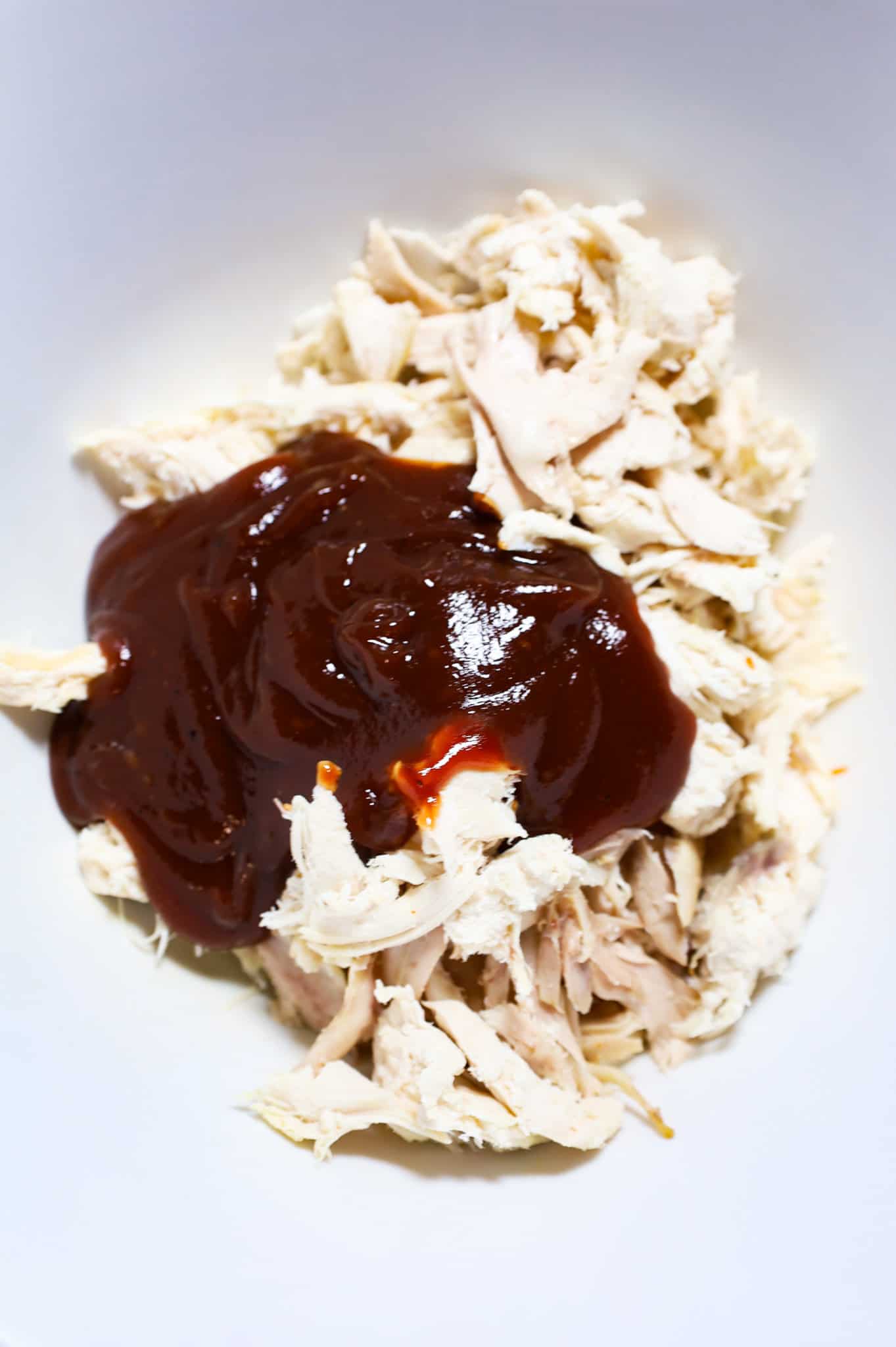 bbq sauce on top of shredded chicken in a mixing bowl