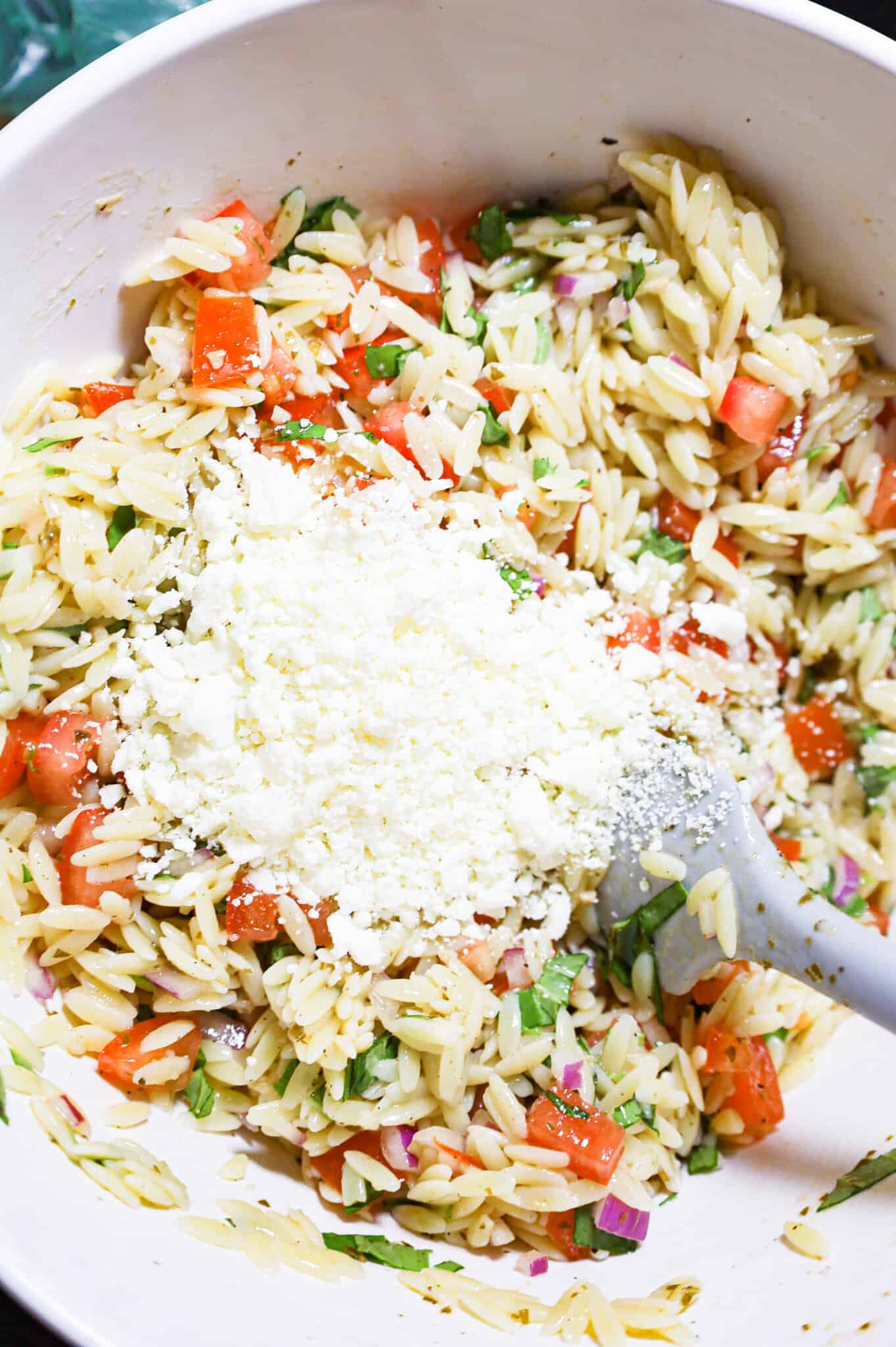 feta cheese on top of orzo pasta salad in a mixing bowl