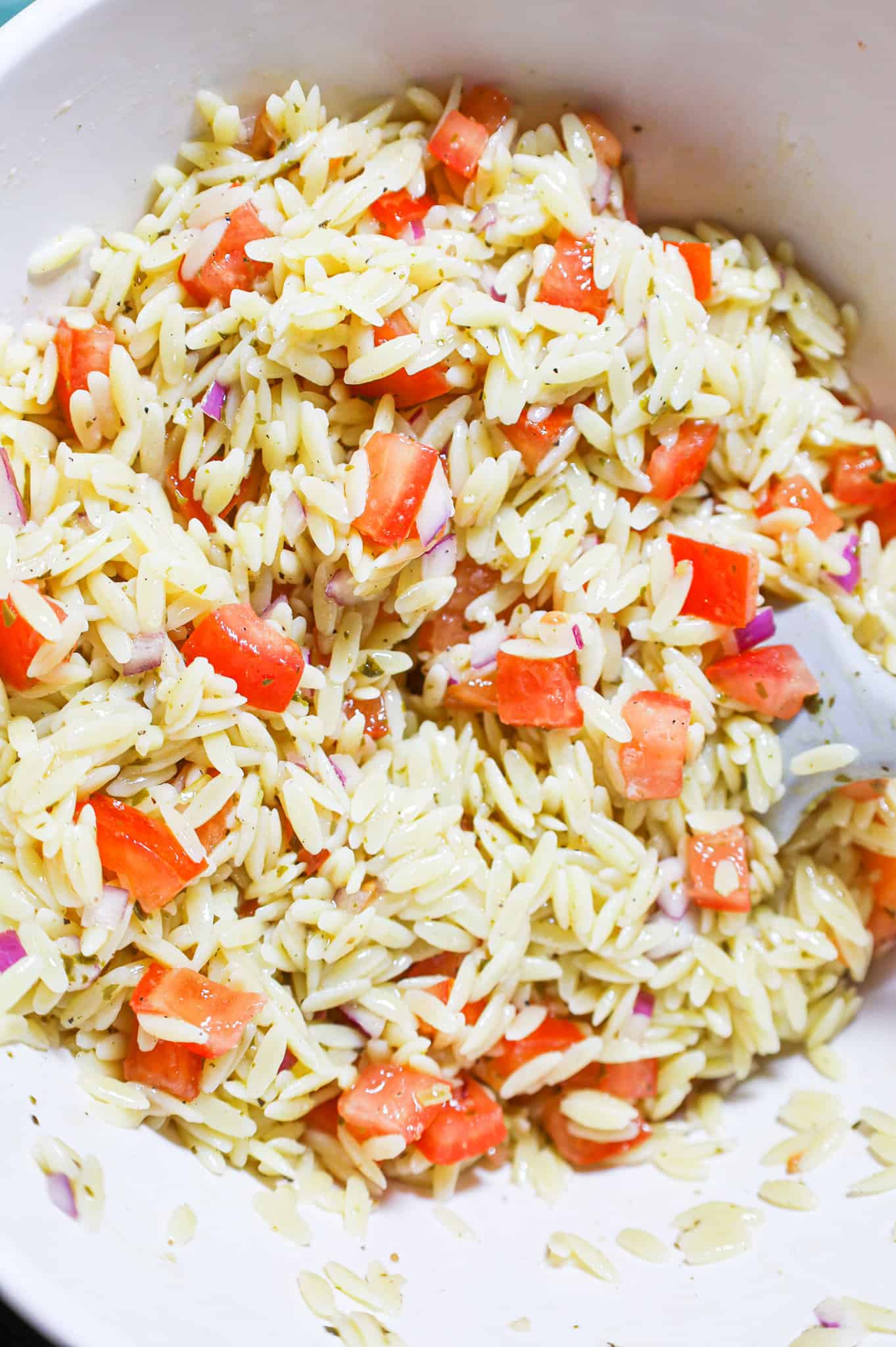 orzo pasta noodles being stirred with tomato bruschetta mixture in a mixing bowl