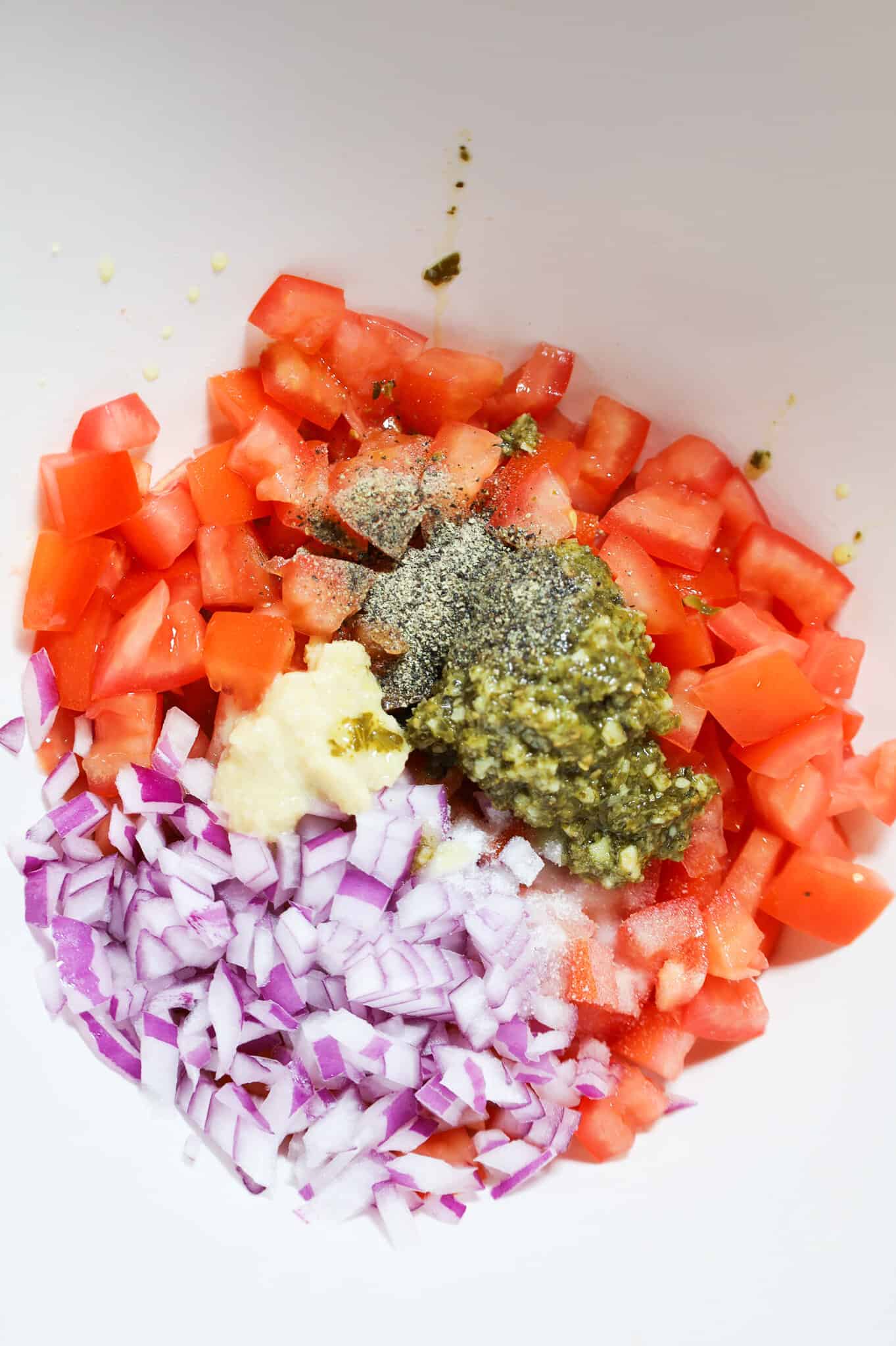 salt,, pepper, garlic puree, basil pesto, diced red onions and diced tomatoes in a mixing bowl