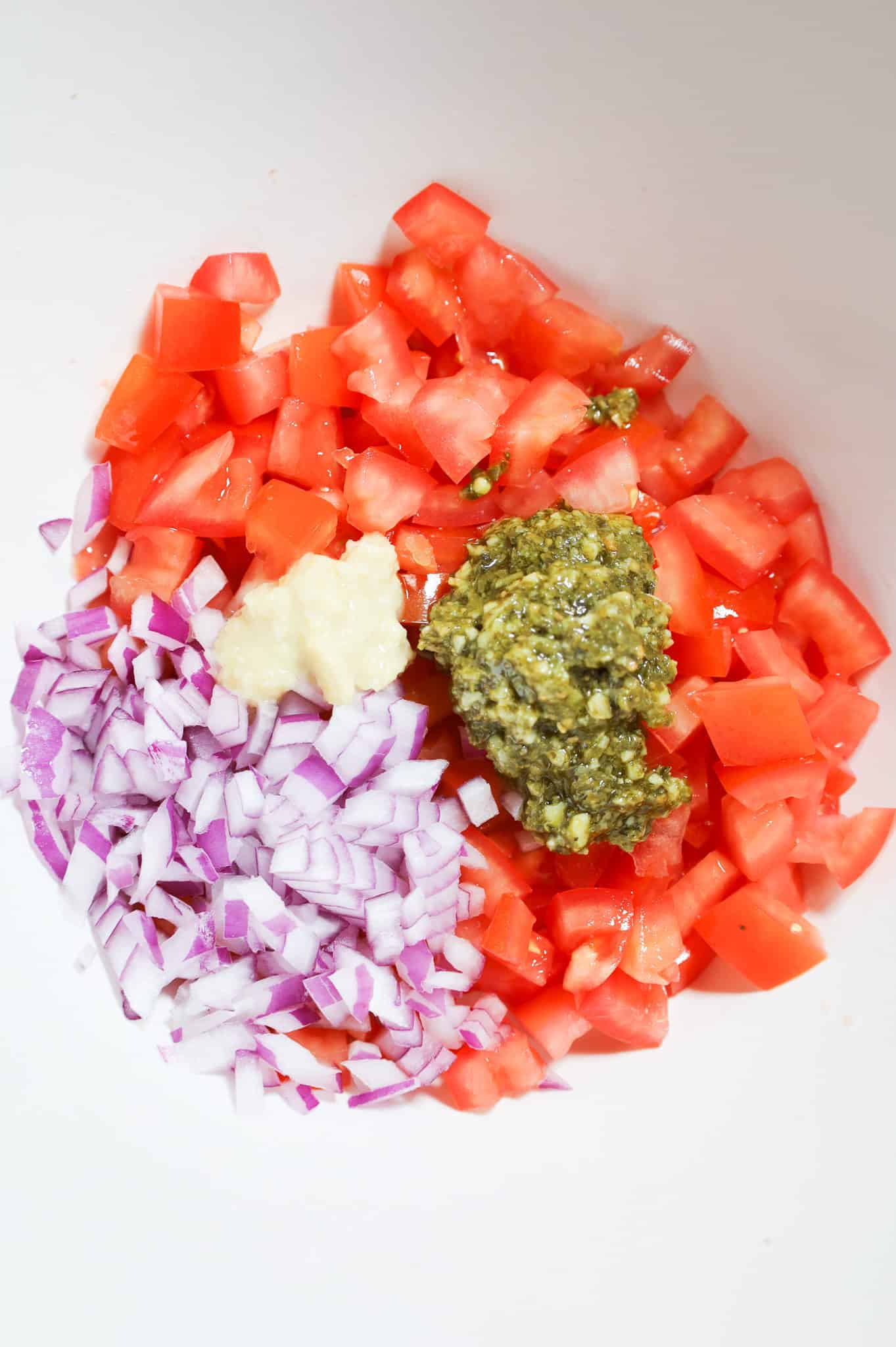 garlic puree, basil pesto, diced tomatoes and diced red onions in a mixing bowl