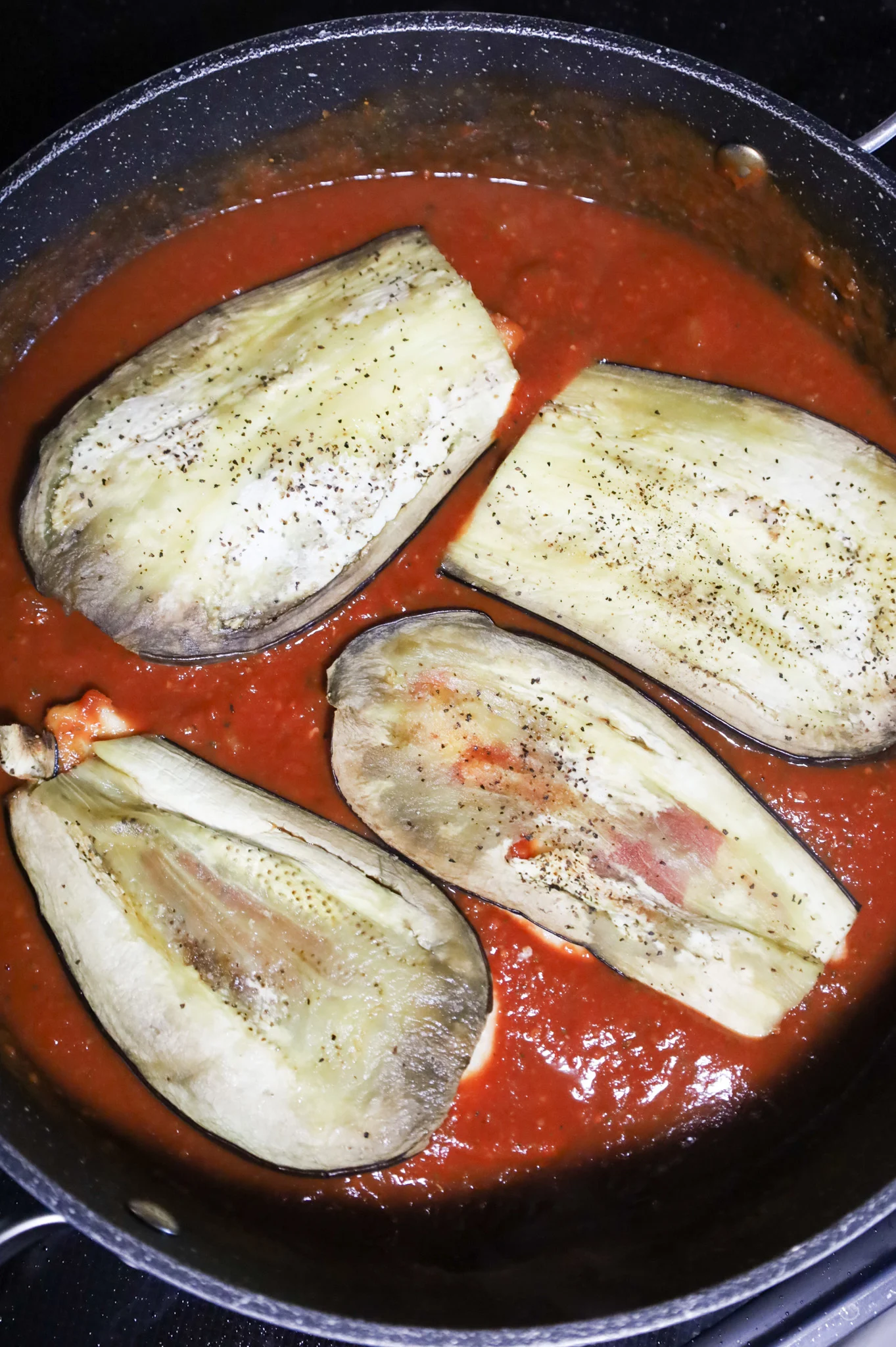 roasted eggplant slices on top of chicken cutlets in a skillet with tomato sauce