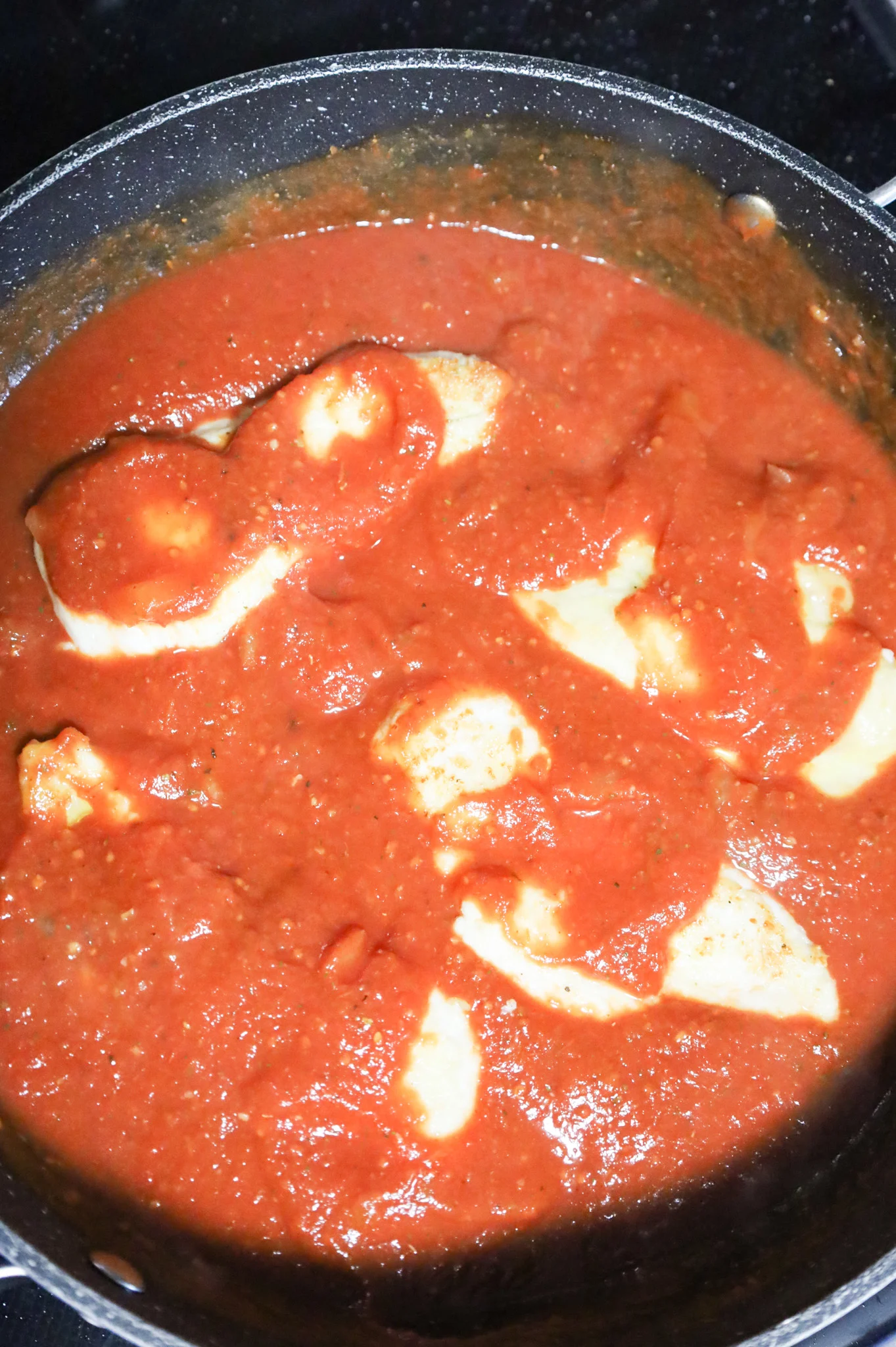 tomato sauce spooned over chicken cutlets in a skillet