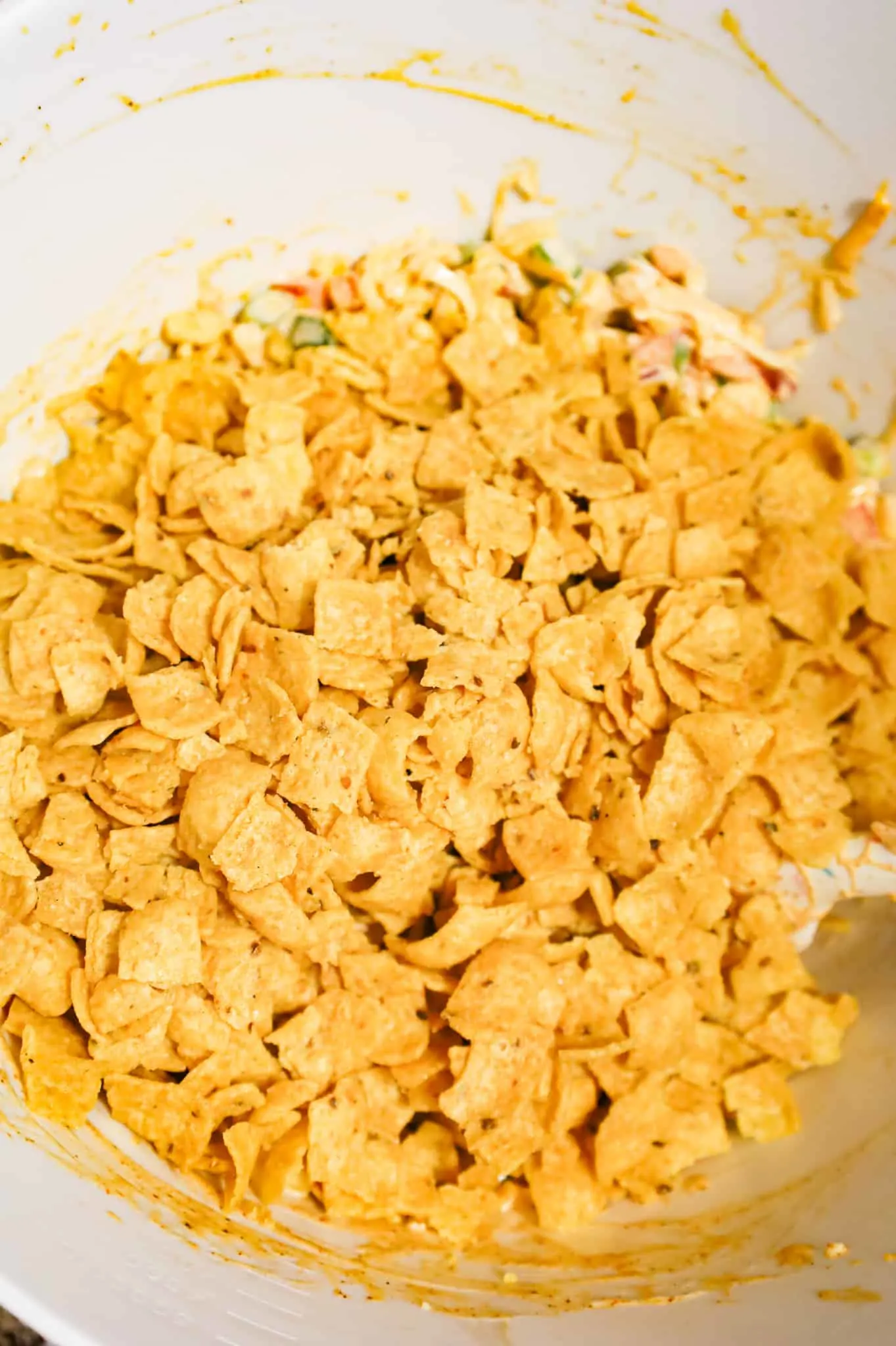 crumbled corn chips on top of cheesy corn salad mixture in a mixing bowl